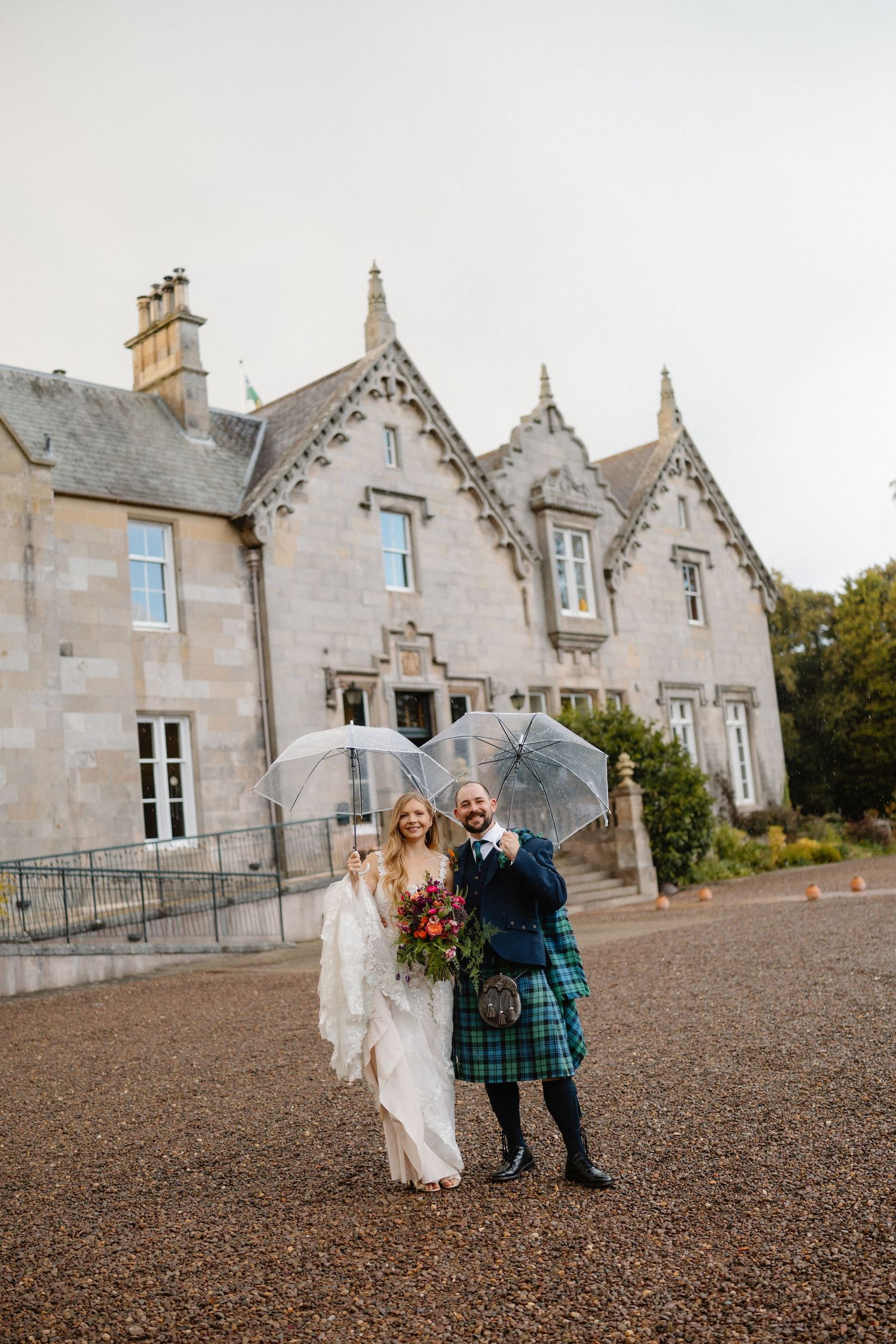 Stone Scottish manor house with gabled roofs serves as backdrop for outdoor celebration on gravel courtyard.