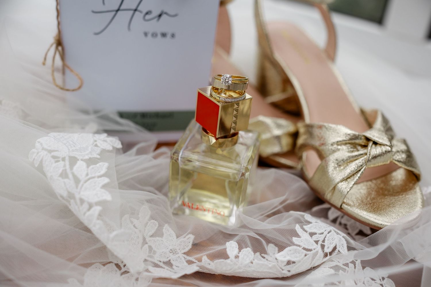 Wedding accessories including perfume bottle and shoes arranged on delicate lace fabric.