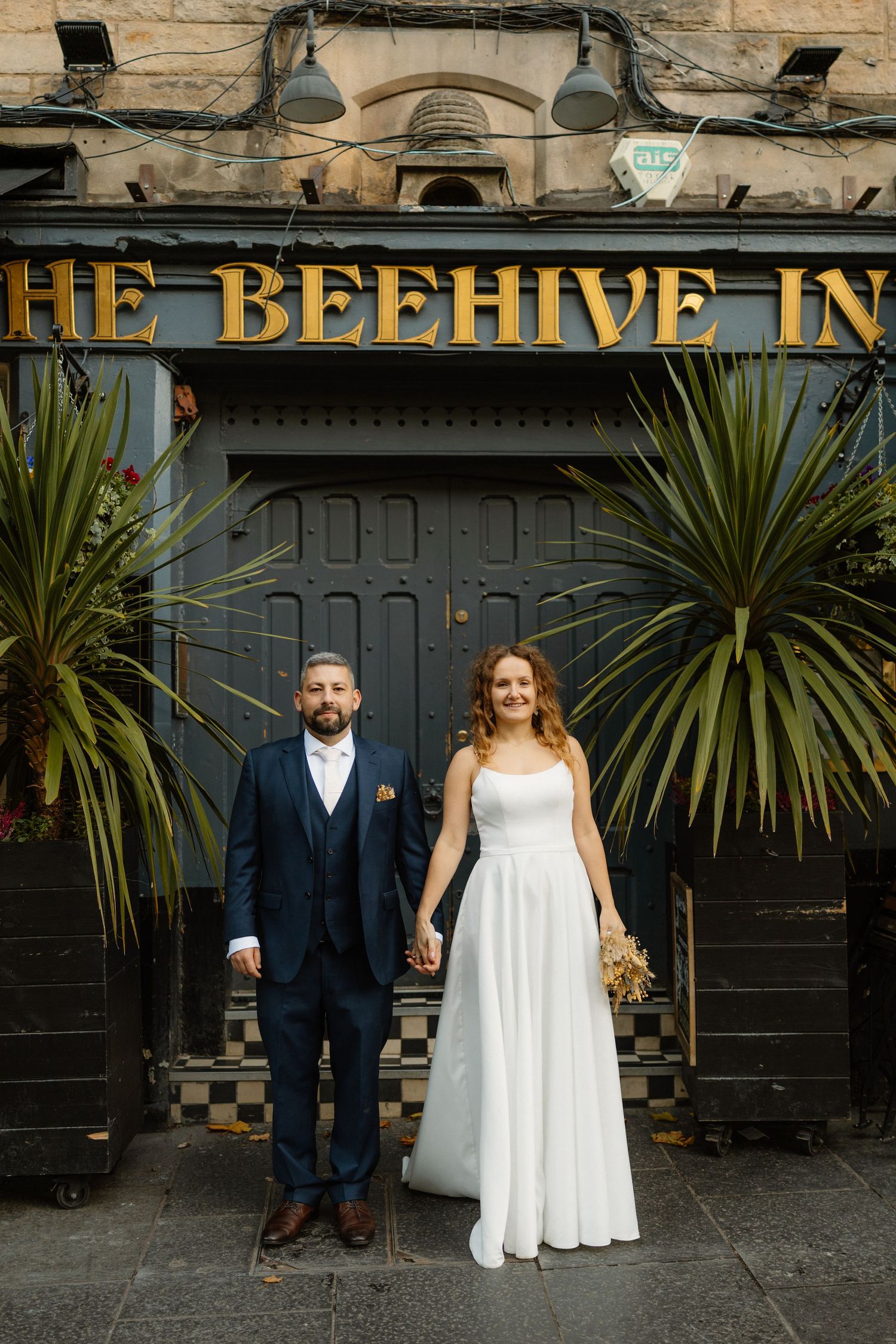Couple poses outside The Beehive Inn with palm plants and checkerboard details.