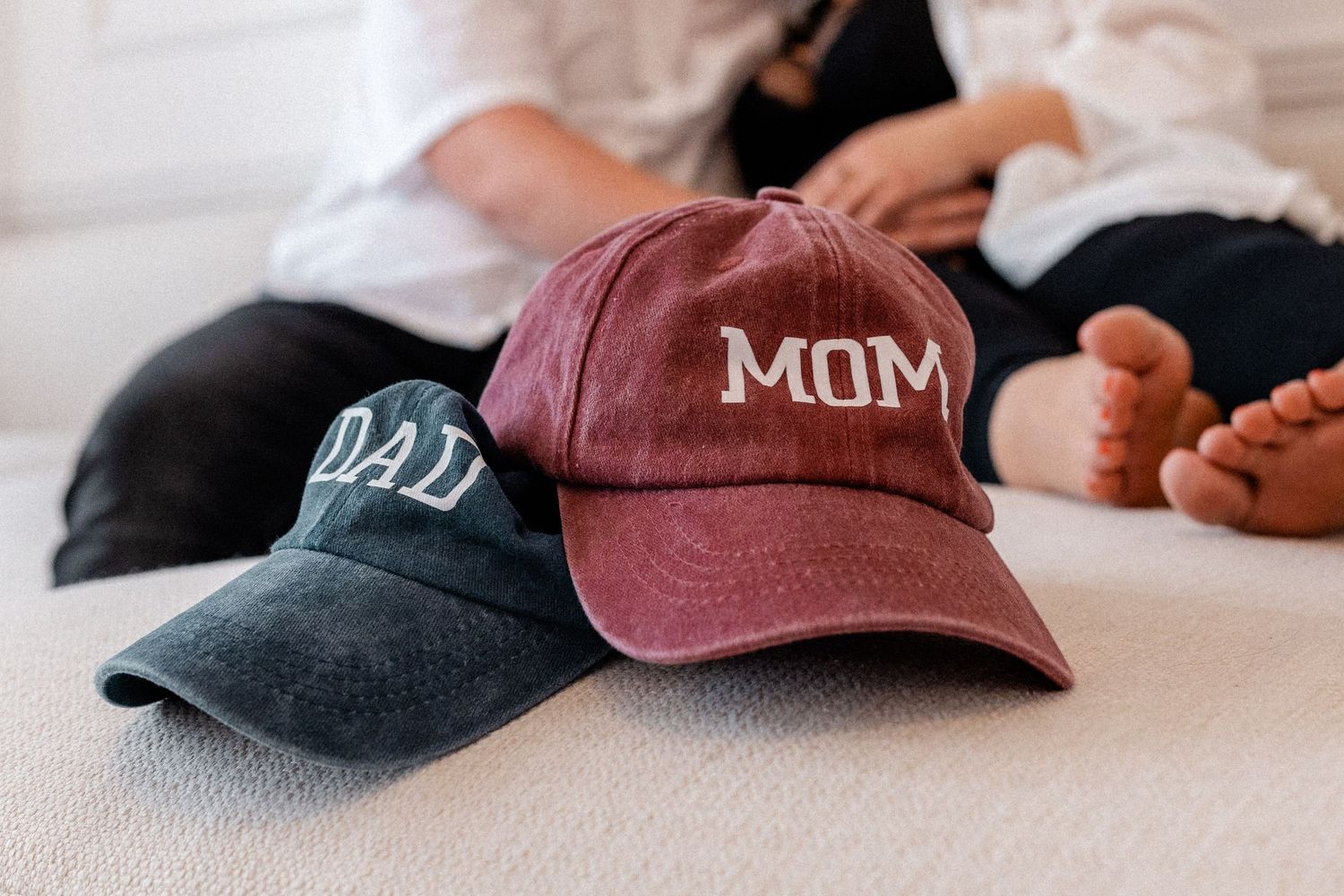 Baseball caps for Mom and Dad arranged on light beige furniture.