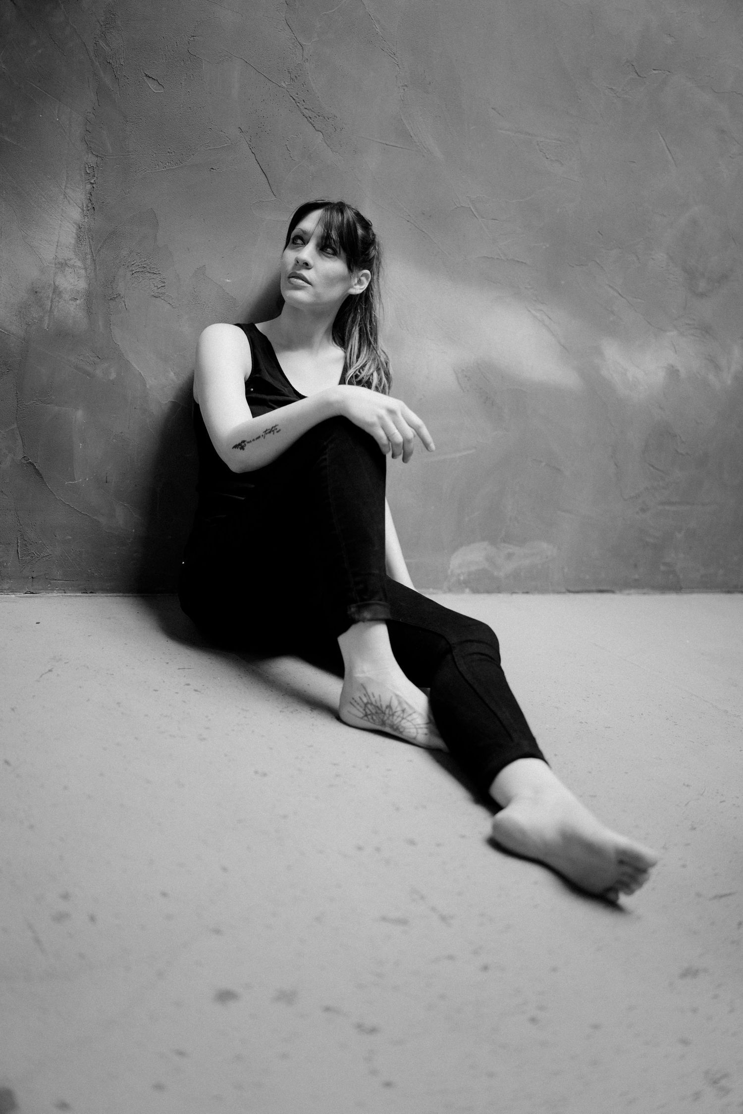 Artistic black and white portrait of person in dark outfit reclining on floor.