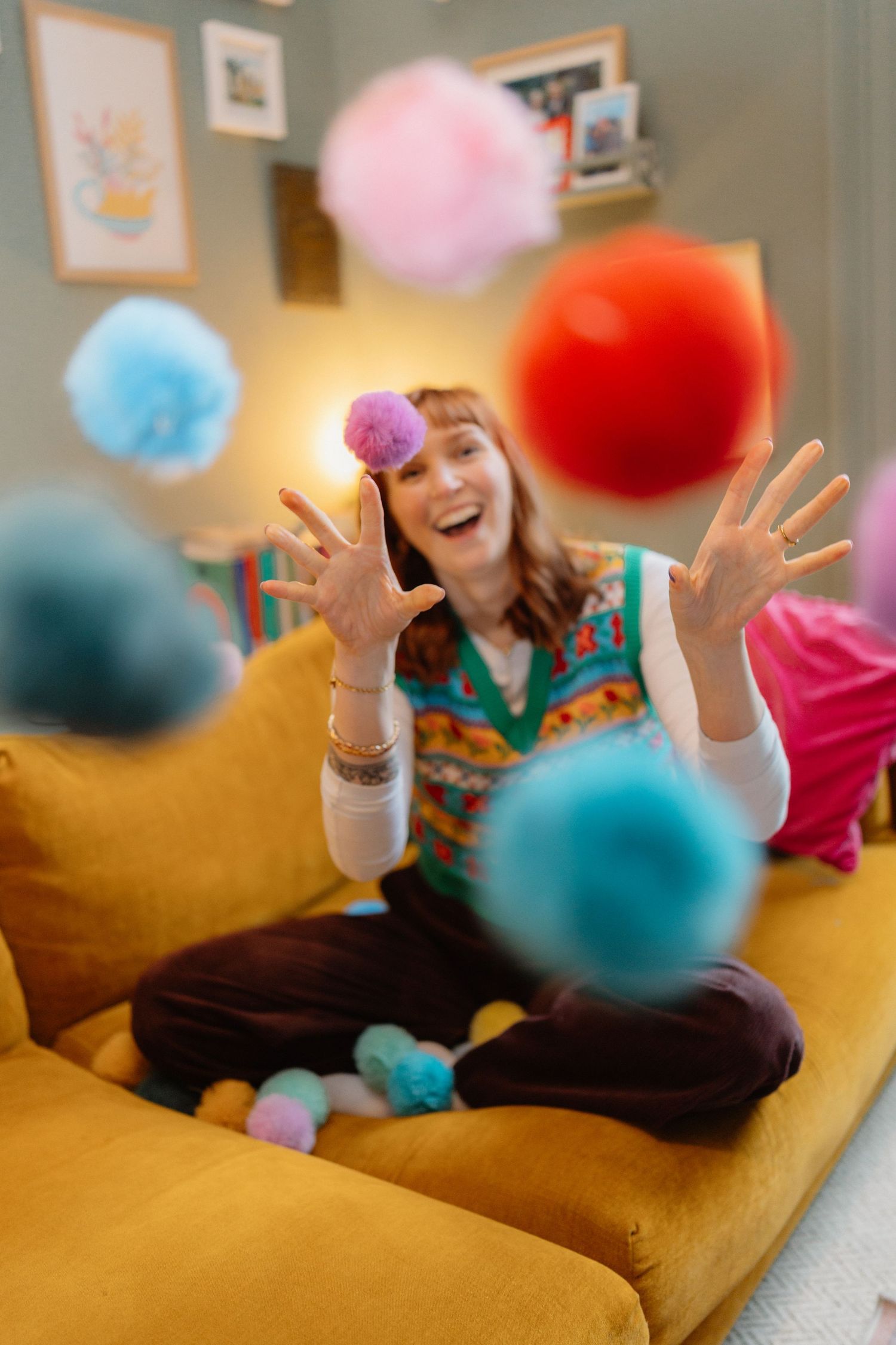 Throwing colorful pom poms in the air while sitting on a yellow couch.