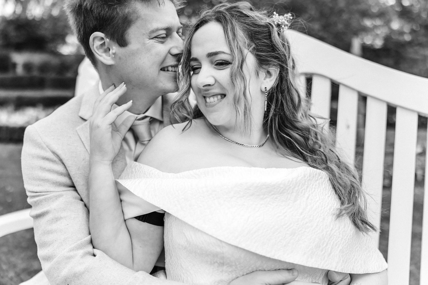 Couple sharing intimate moment on white bench in garden setting.