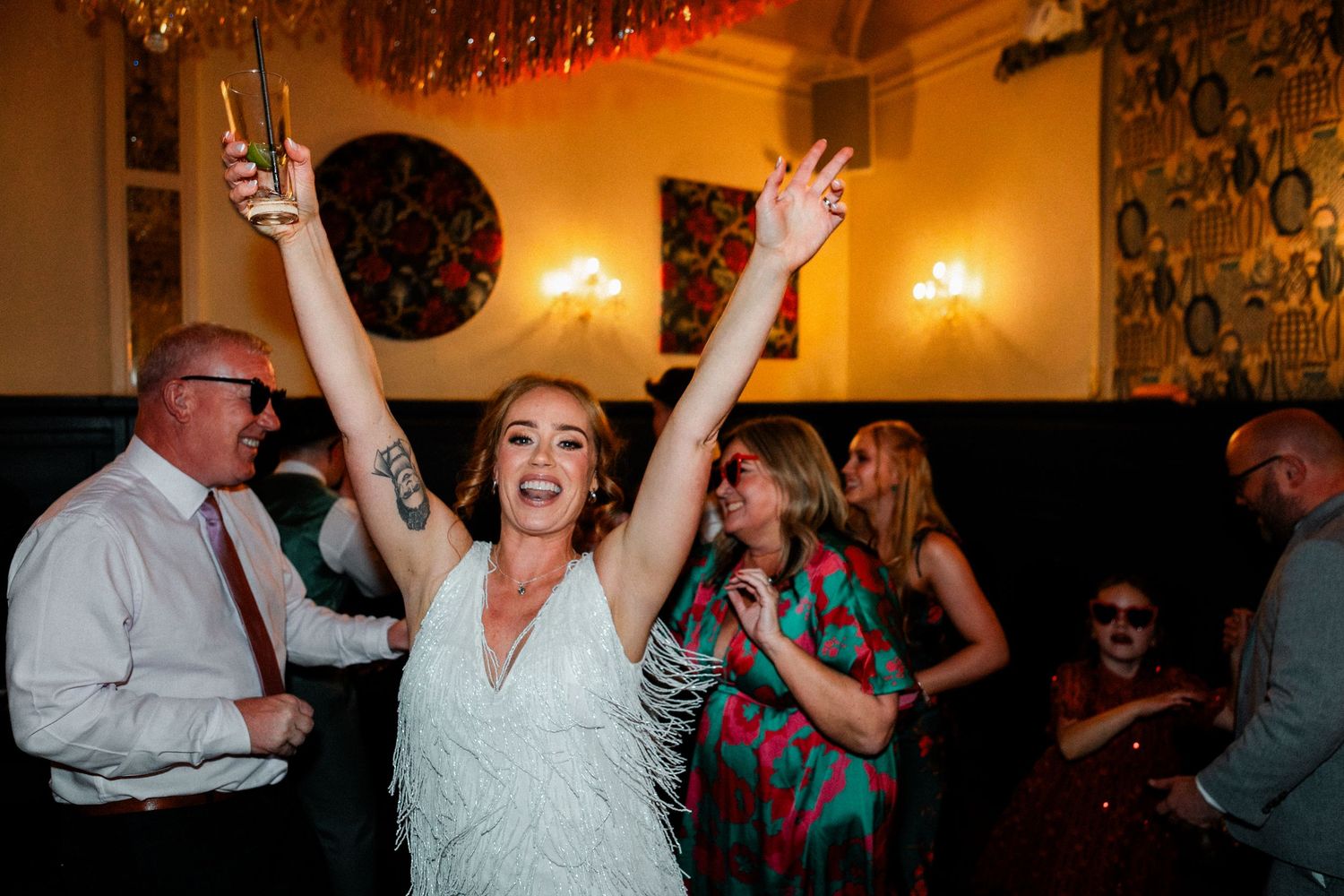 Wedding guests dancing and celebrating on a dimly lit dance floor with string lights overhead.