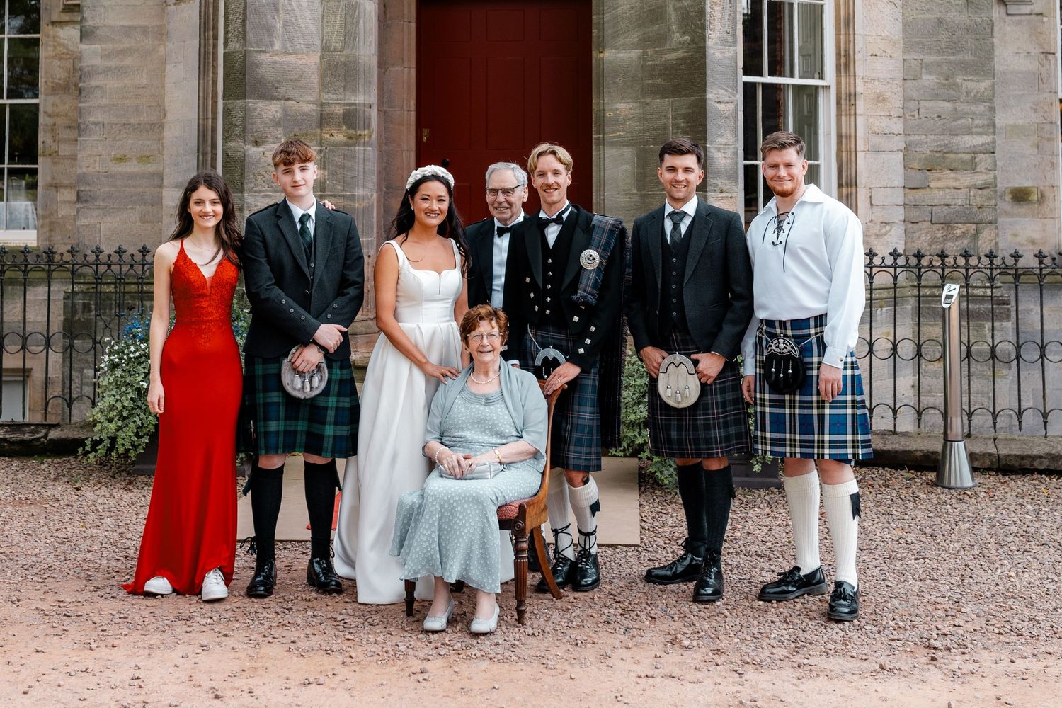 Wedding party members arranged in formal attire outside a grand stone building entrance.