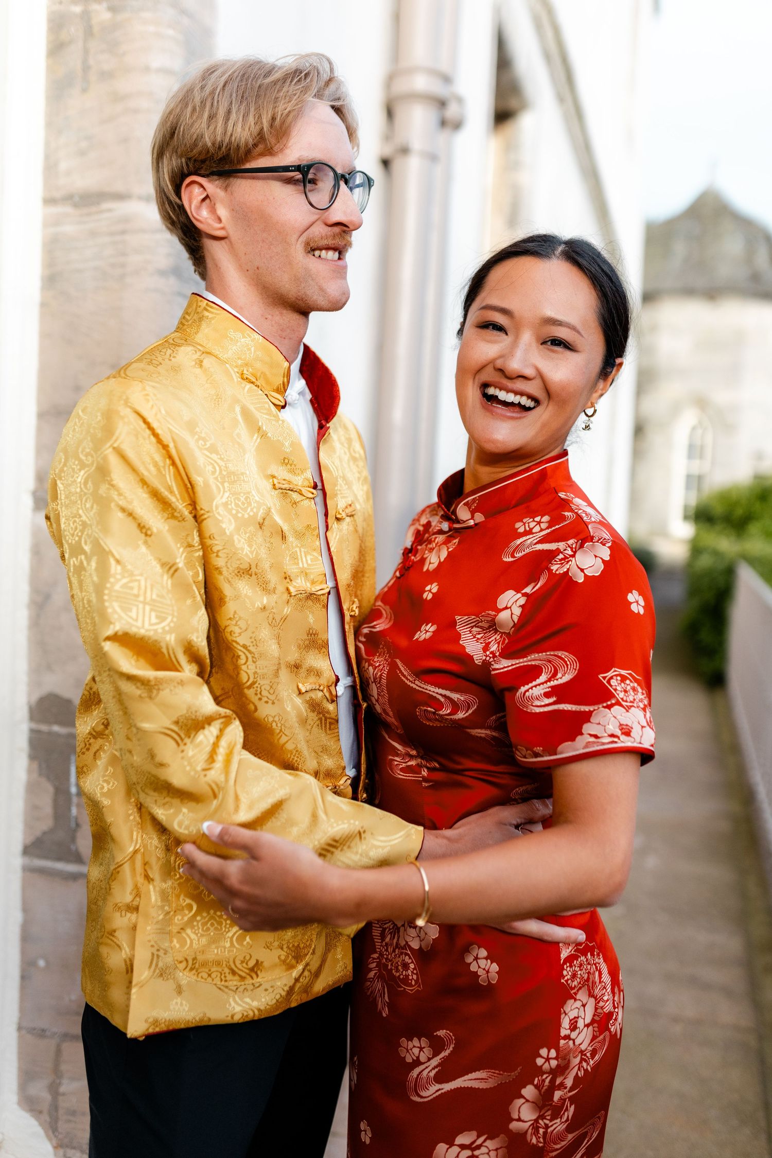 Couple embracing and laughing, wearing traditional Chinese formal attire in yellow and red.