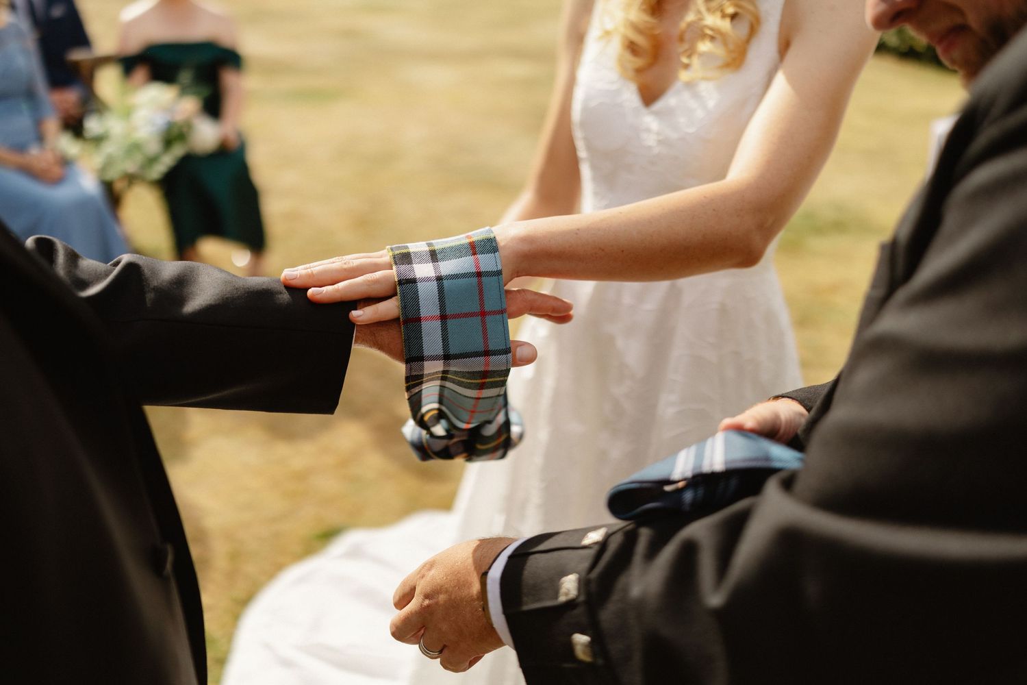 Handfasting ceremony with blue tartan ribbon binding couple's hands at outdoor Scottish wedding.