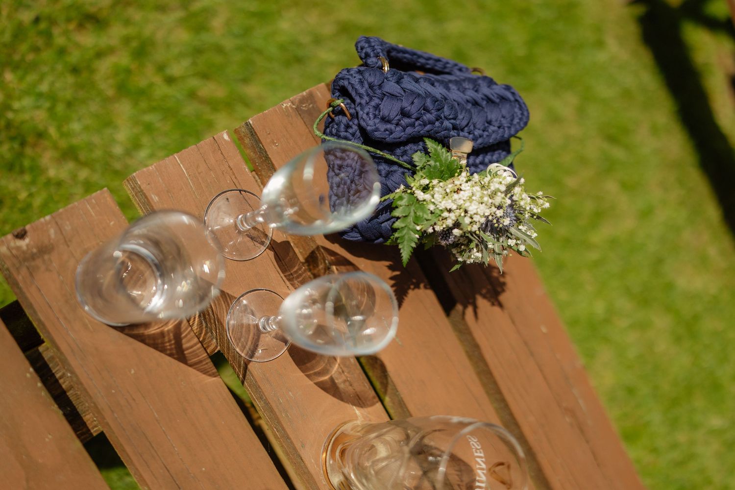 Empty wine glasses and floral arrangement on a wooden pallet table at an outdoor wedding.