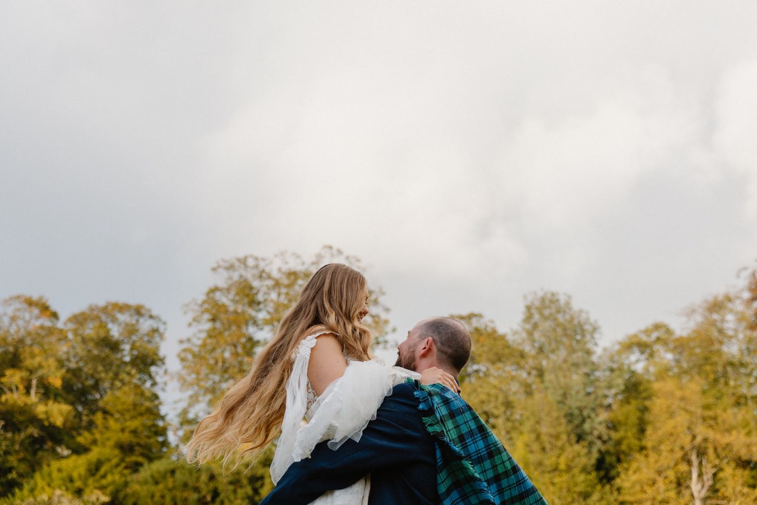 Two people embrace in a field at sunset with golden light streaming through trees in the background.