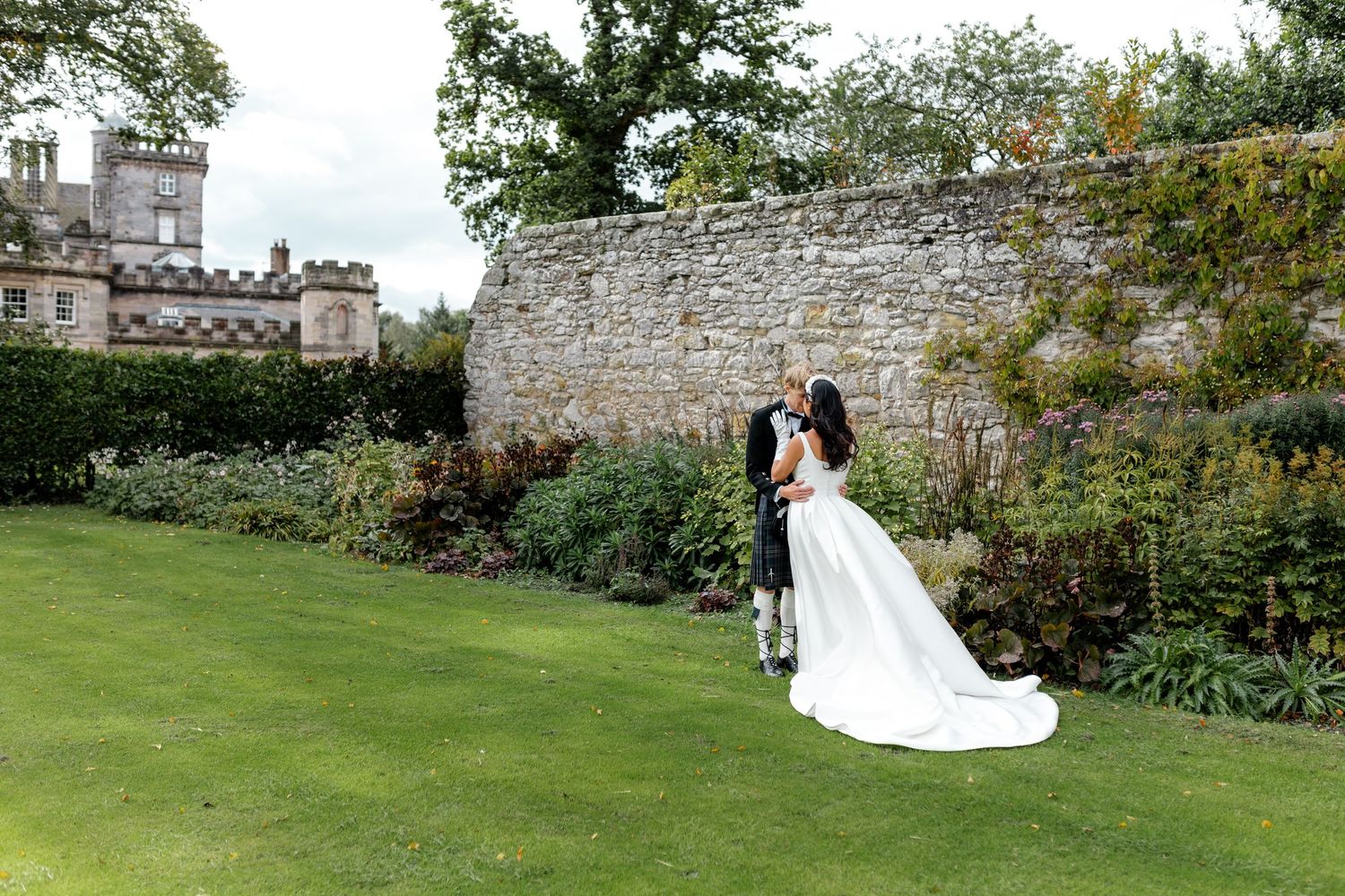A couple poses for romantic wedding photos in a beautiful castle garden setting with stone walls and lush greenery.