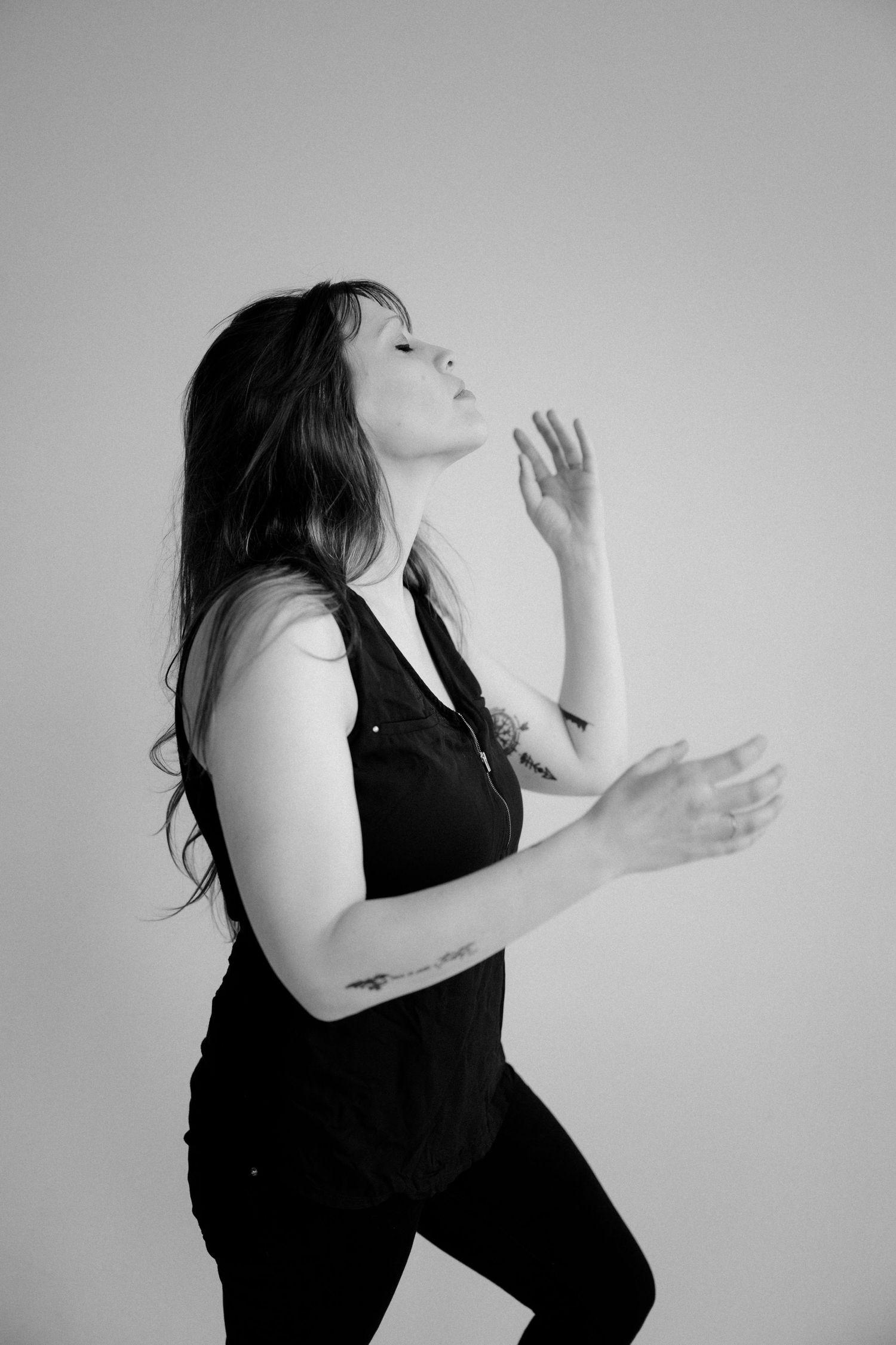 Dramatic black and white photo of person in dark outfit with expressive hand gestures.