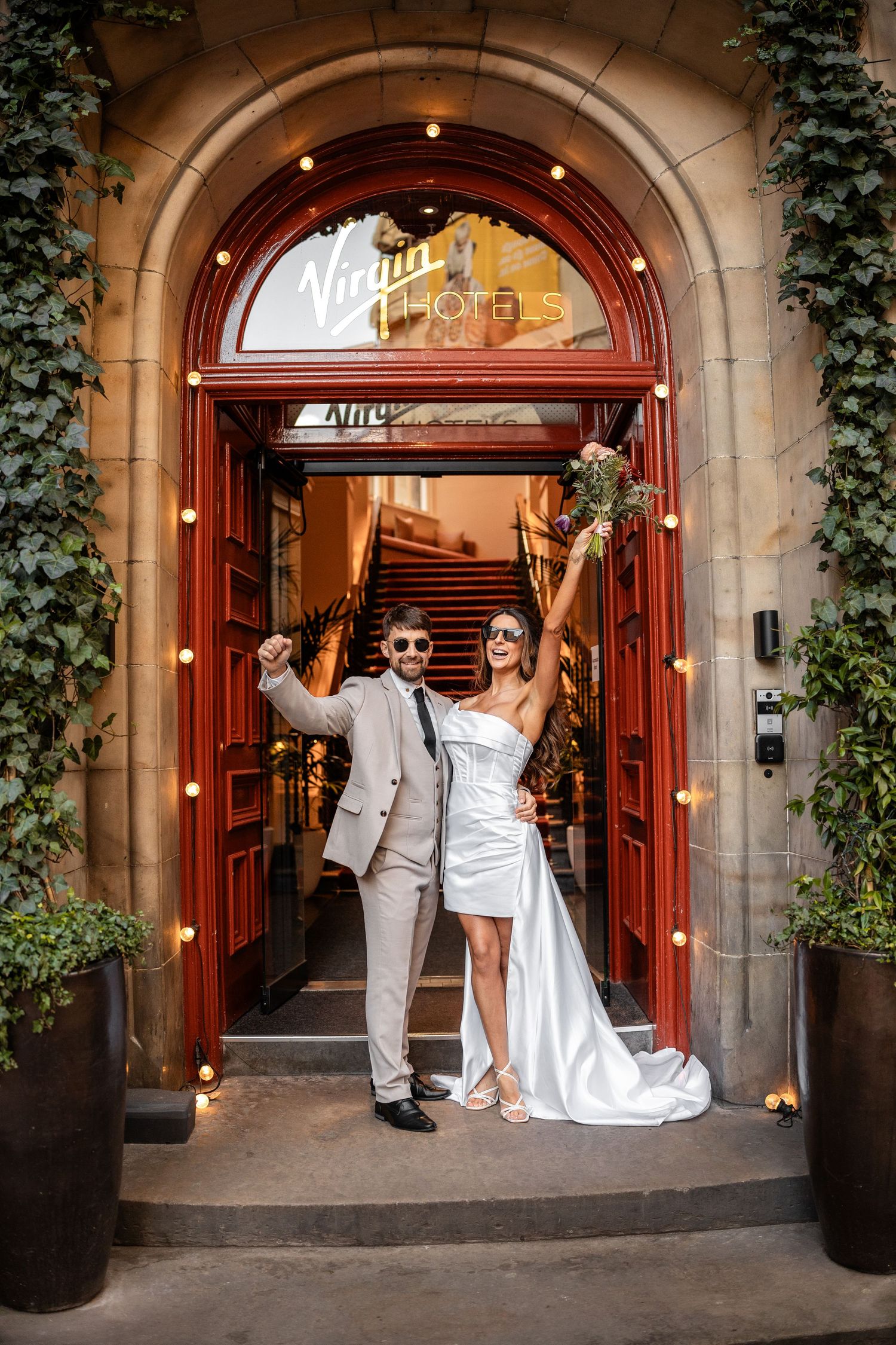 Wedding couple poses in front of an illuminated archway entrance with ivy-covered walls.