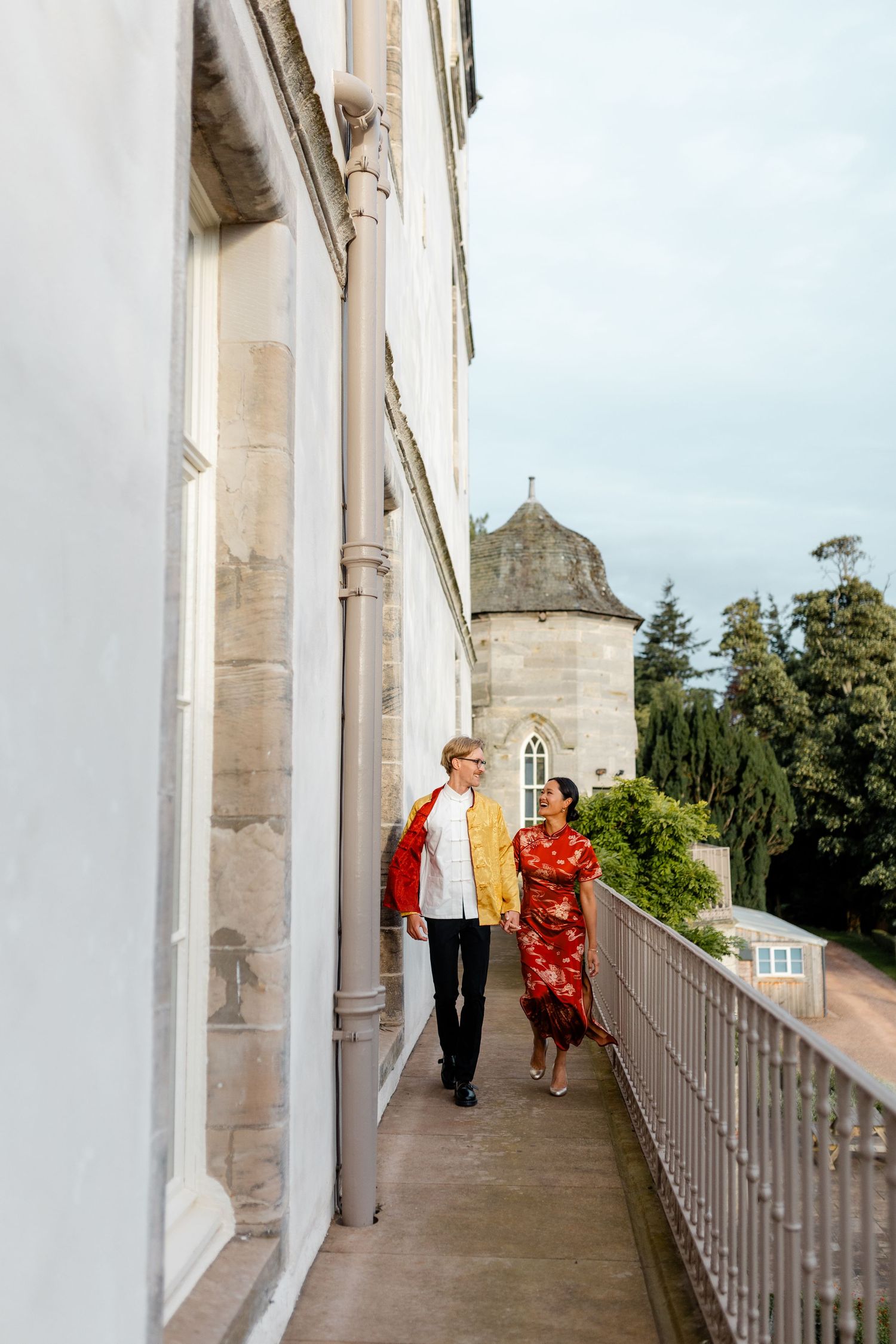 Couple walking and laughing along a white columned balcony.