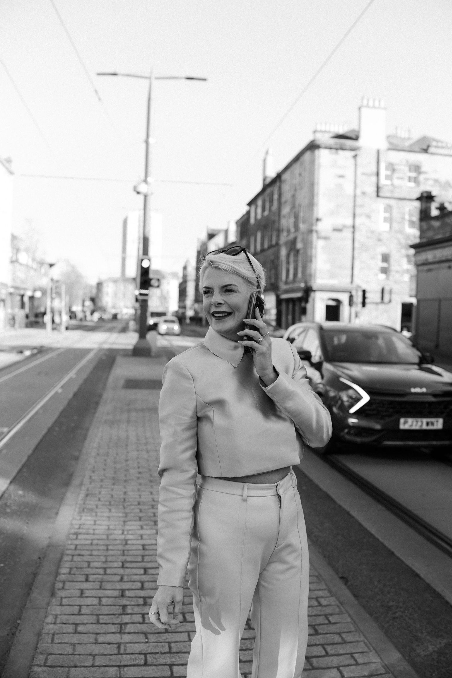 A person in light-colored clothing poses playfully on a brick sidewalk in an urban setting.