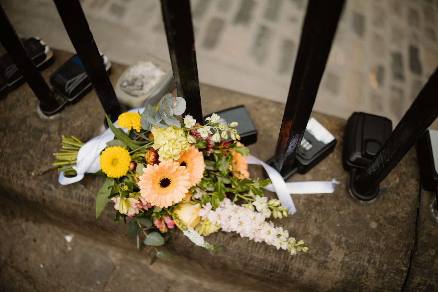 Bridal bouquet with yellow gerberas and white flowers resting on stone steps near black iron railings.