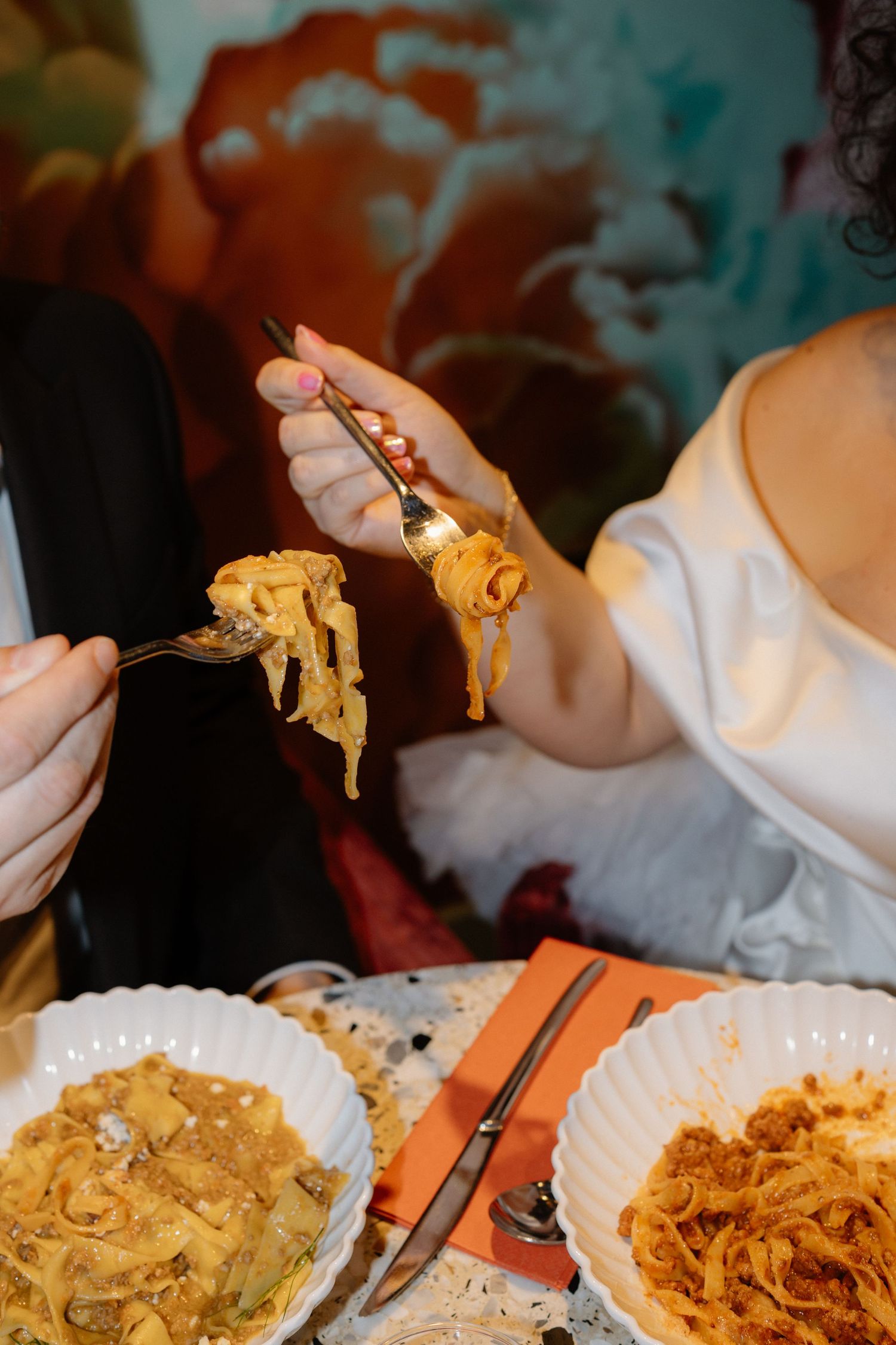 Bride in white dress sharing pasta dish with groom at wedding reception dinner table.