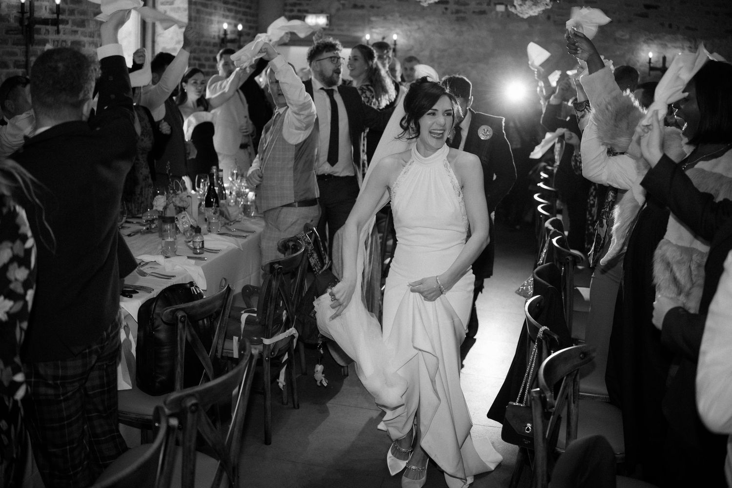 Bride in white gown walks through cheering guests at elegant black and white wedding reception celebration.