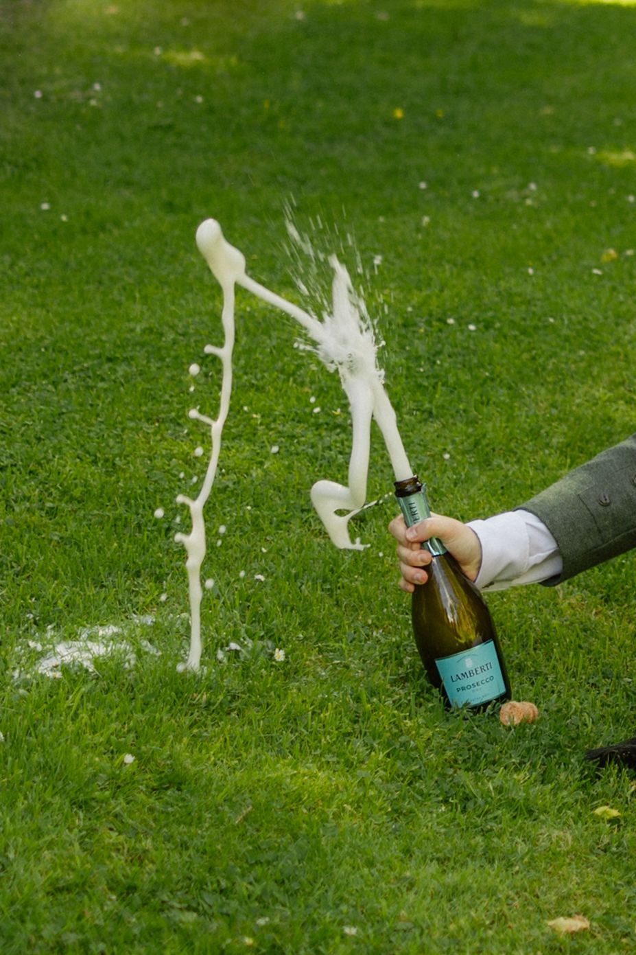 Champagne bottle being opened on grass, with bubbly liquid splashing dramatically in the air outdoors.