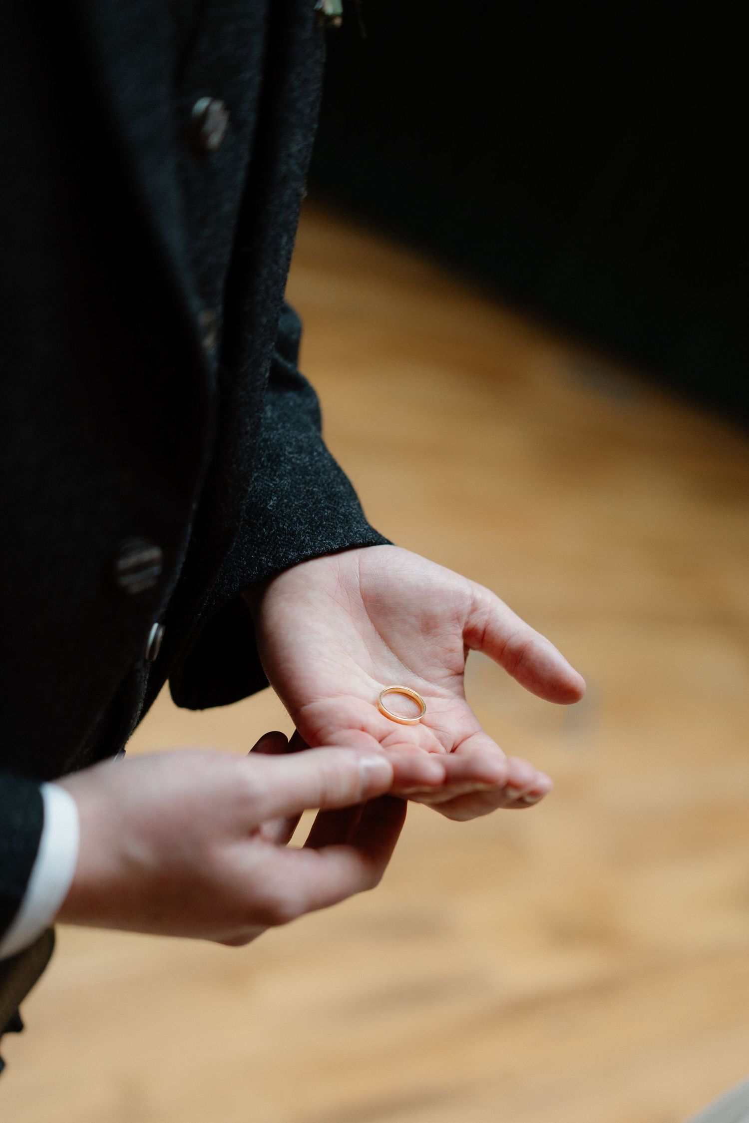 Close-up of hands holding a gold wedding ring during a wedding ceremony exchange.