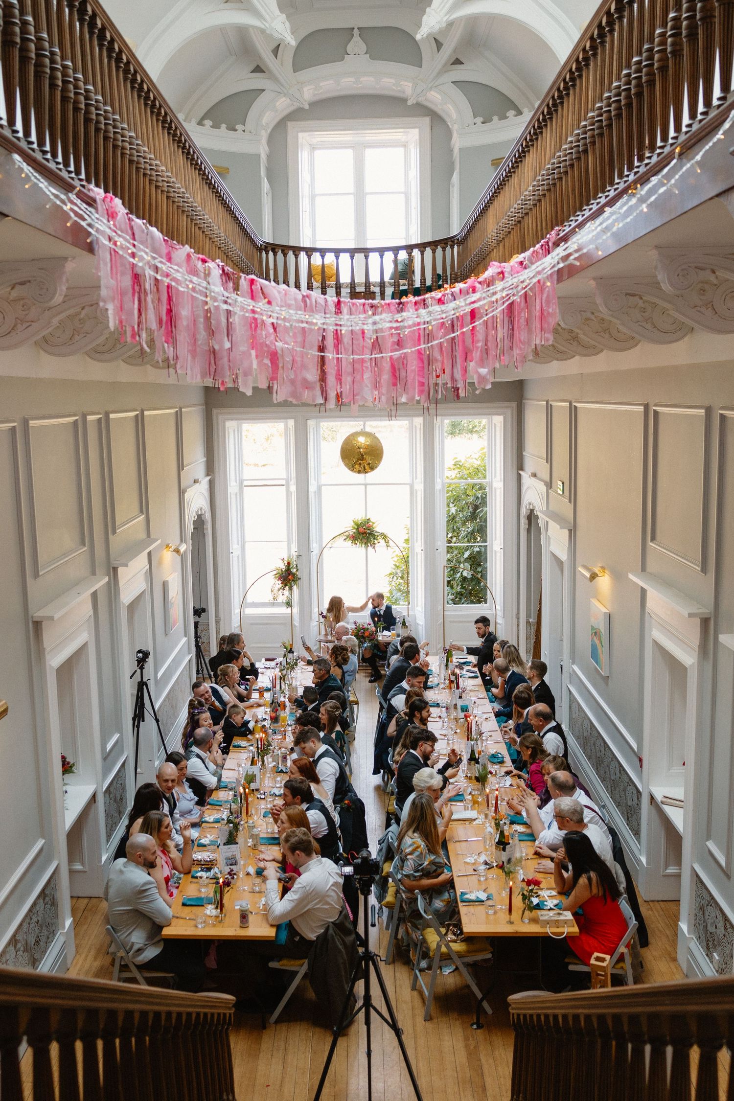 Aerial view of wedding reception with long tables, pink tassel decorations, and a gold disco ball.
