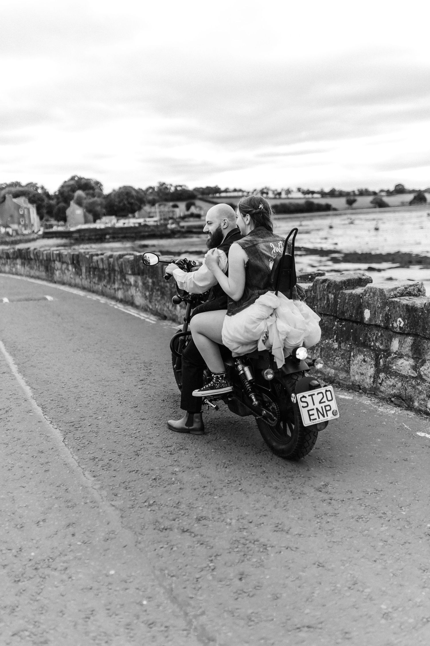 Creative black and white sequence of newlyweds posing on a vintage motorcycle along a coastal road.