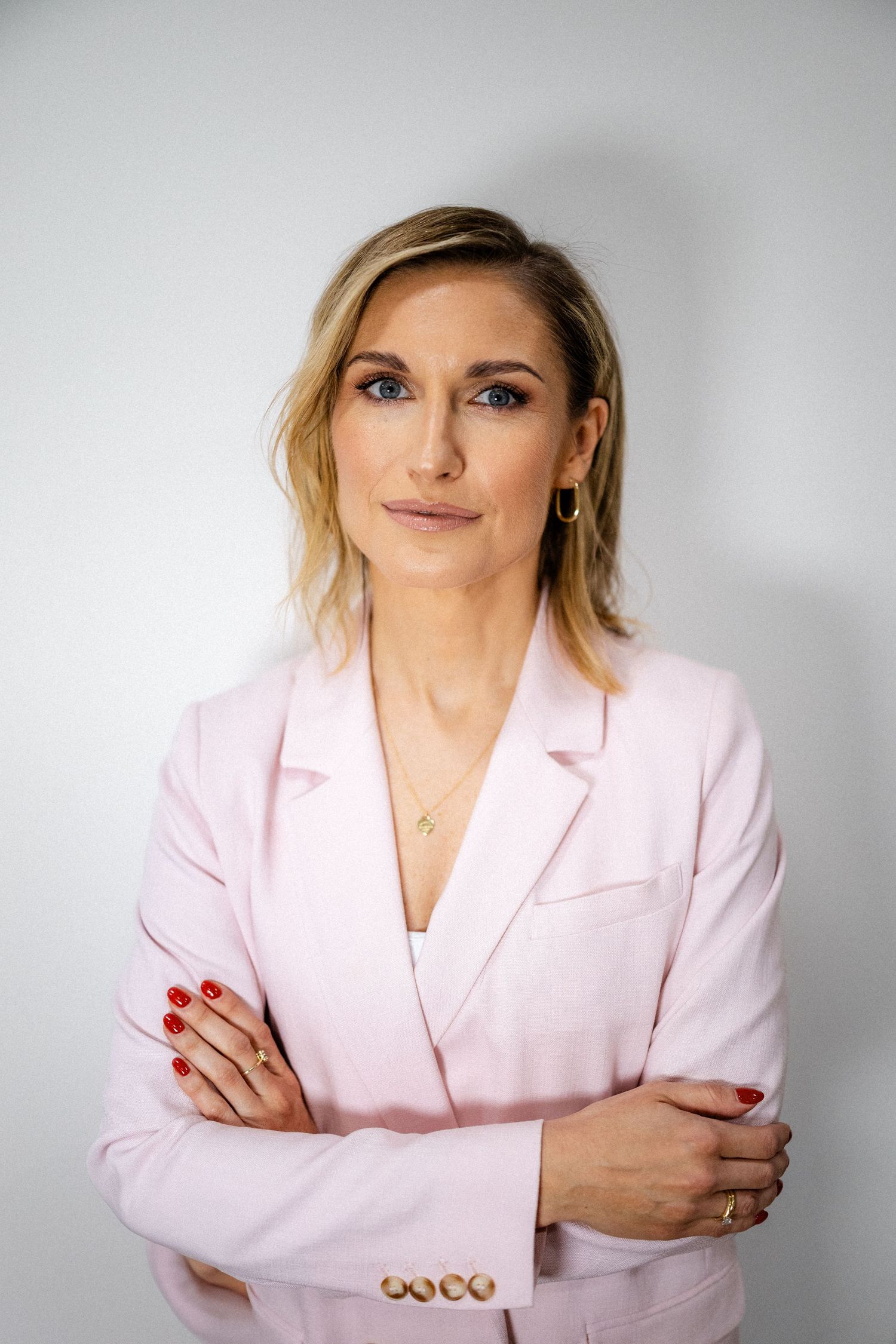 Professional portrait of someone wearing a light pink blazer against a white background.