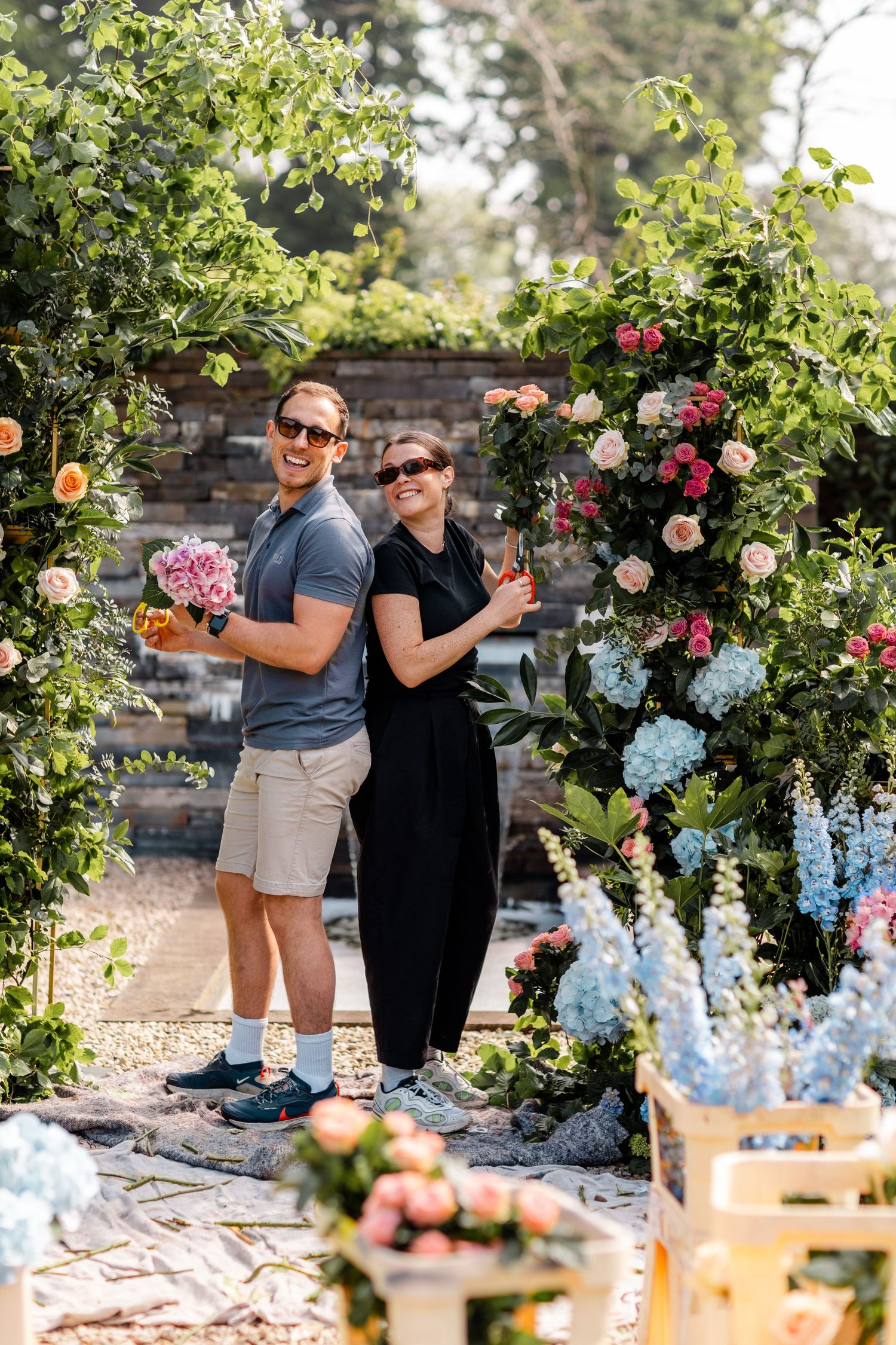 Outdoor party setup with floral arrangements and blue hydrangeas against stone wall.