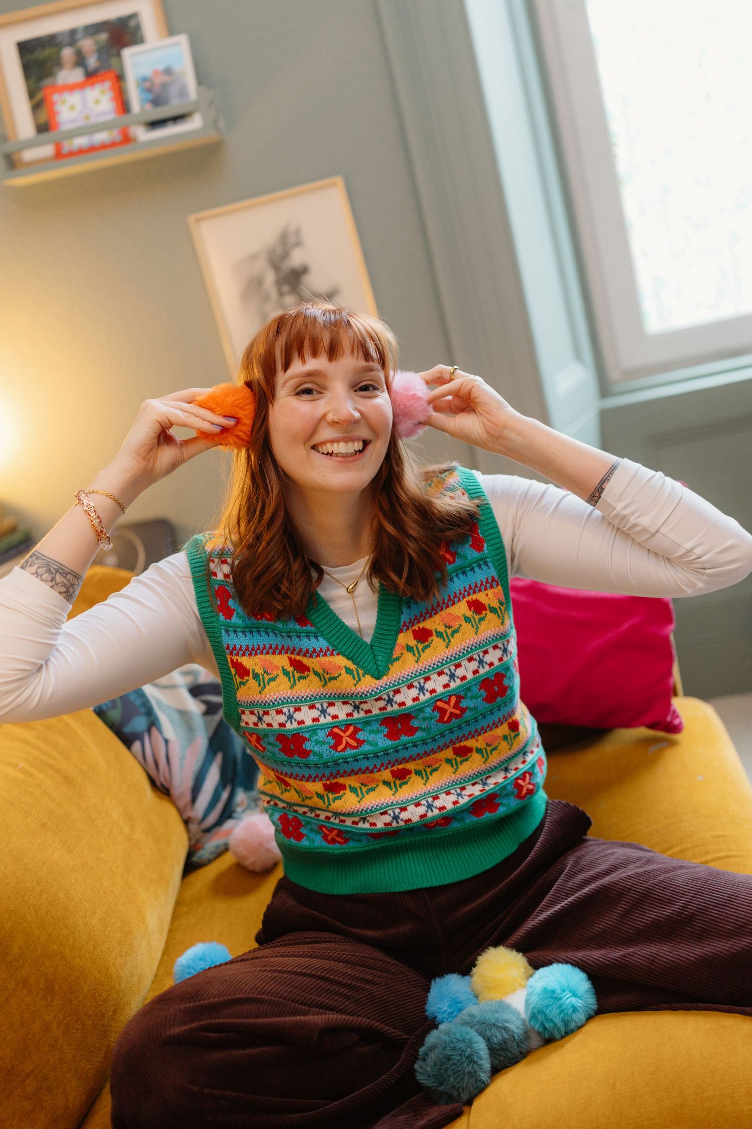 Energetic poses on a mustard yellow couch wearing a festive patterned sweater vest.
