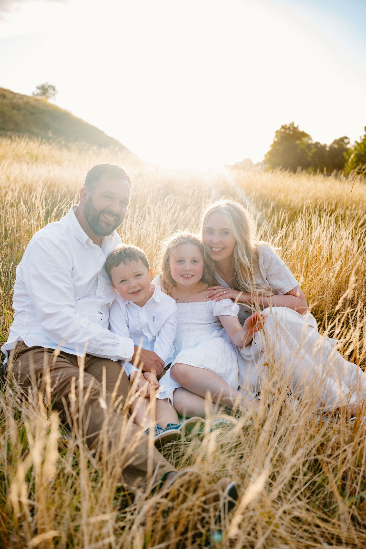 Family sitting together in golden sunlit field of tall grass during sunset.