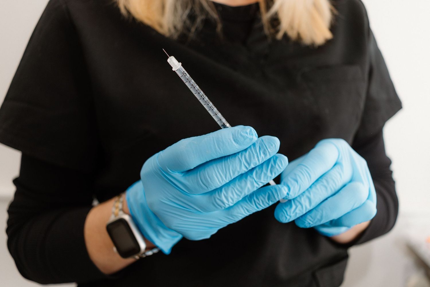 Medical professional in black clothing and blue gloves preparing injection materials.