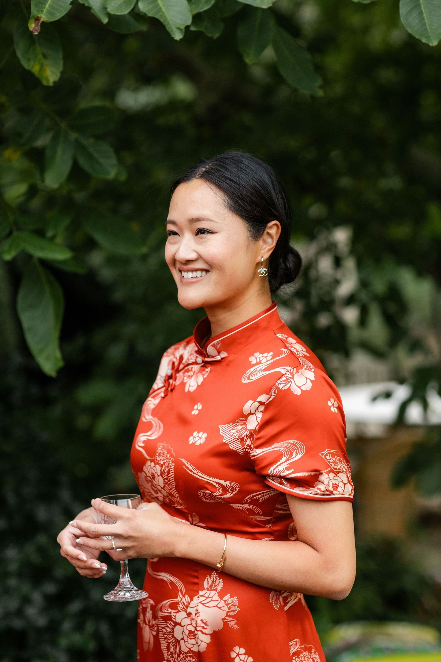 Person in red traditional Chinese qipao dress holding a wine glass outdoors.