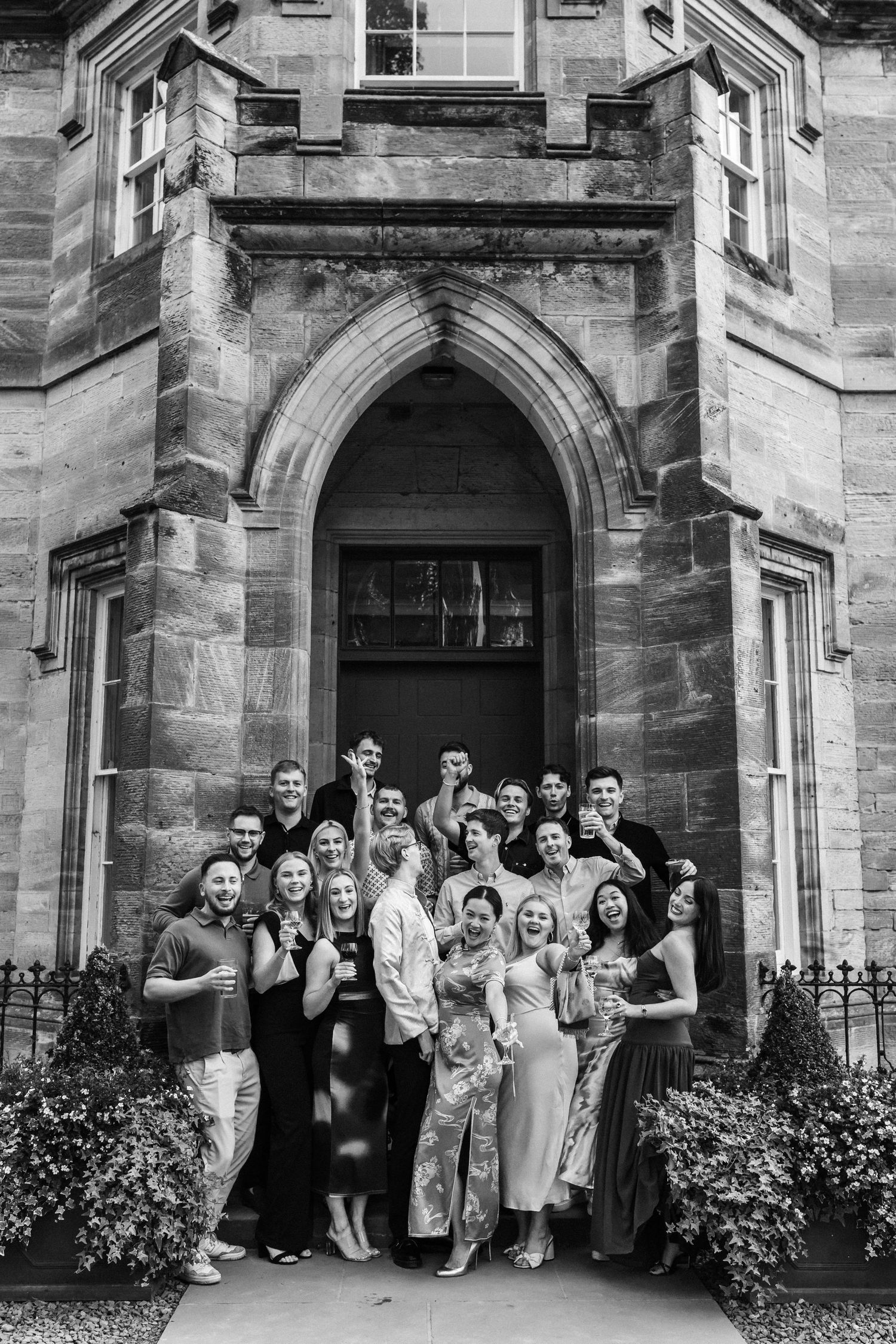 A black and white group photo of wedding guests gathered in a gothic stone doorway.