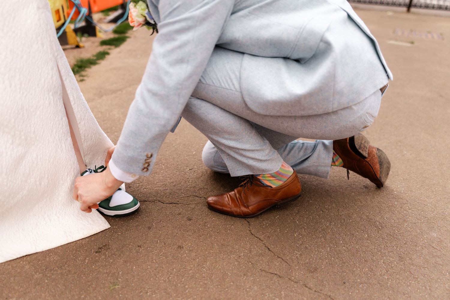 Close-up of formal shoes and flowing white dress hem on pavement.