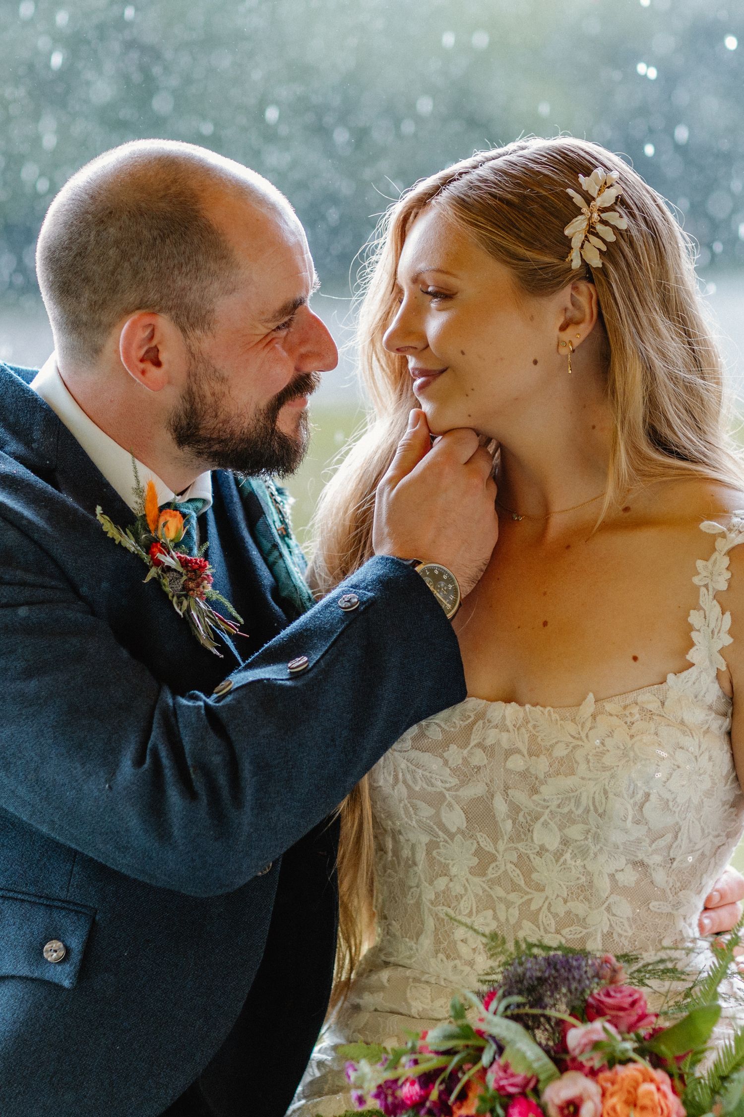 A tender wedding moment captured with a beautiful lace dress, colorful bouquet and soft falling snow in the background.