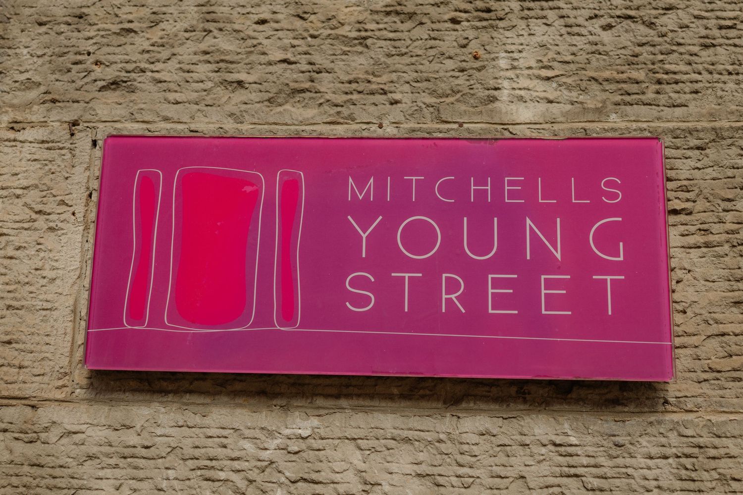 Pink sign reading Mitchells Young Street mounted on a stone wall.