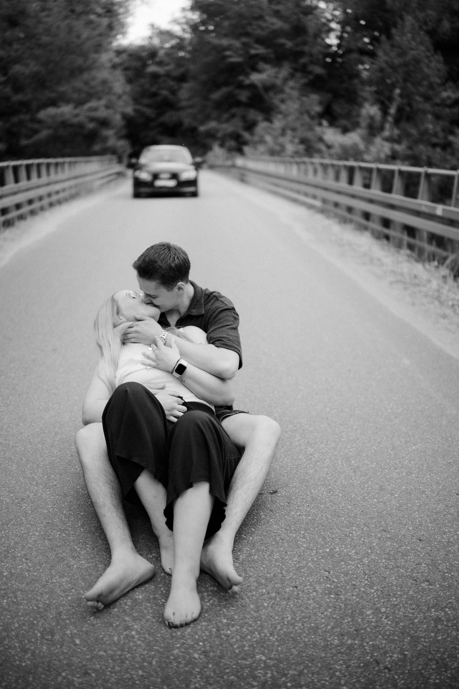 Two people lie intimately on an empty road in a black and white photograph.