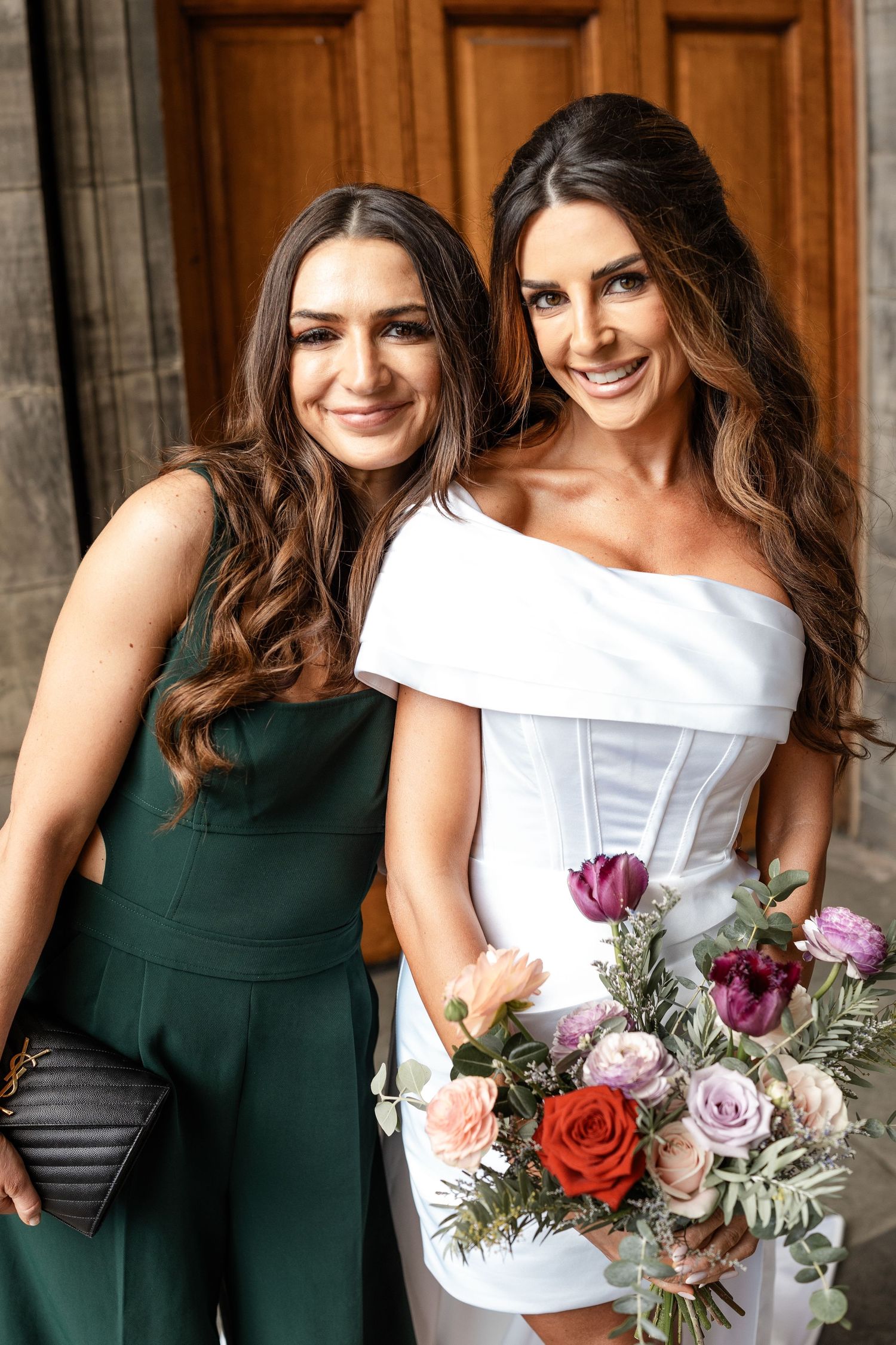 Wedding party in dark green and white dresses holding floral bouquets.