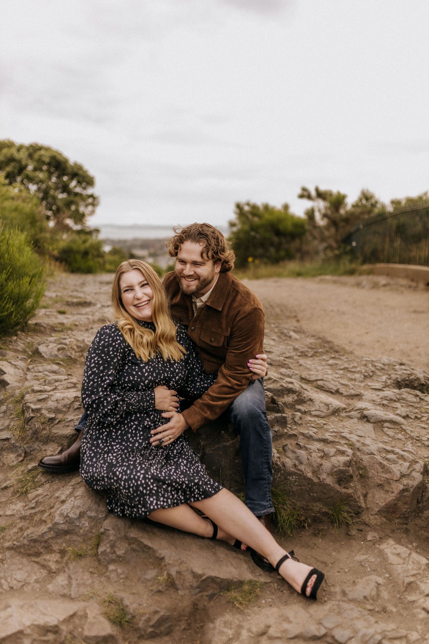 A couple sits together on rocky terrain during a romantic outdoor photoshoot.