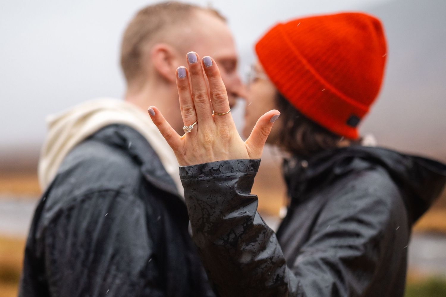 Two people embracing and kissing while wearing winter coats and a bright orange beanie.