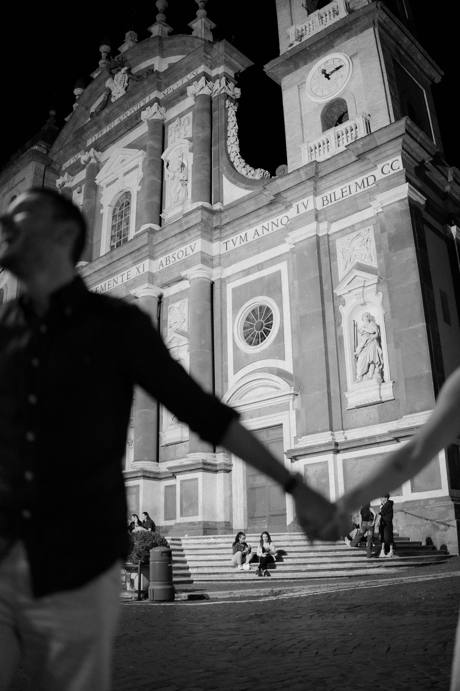 Dramatic black and white nighttime view of an illuminated church facade with people on steps.