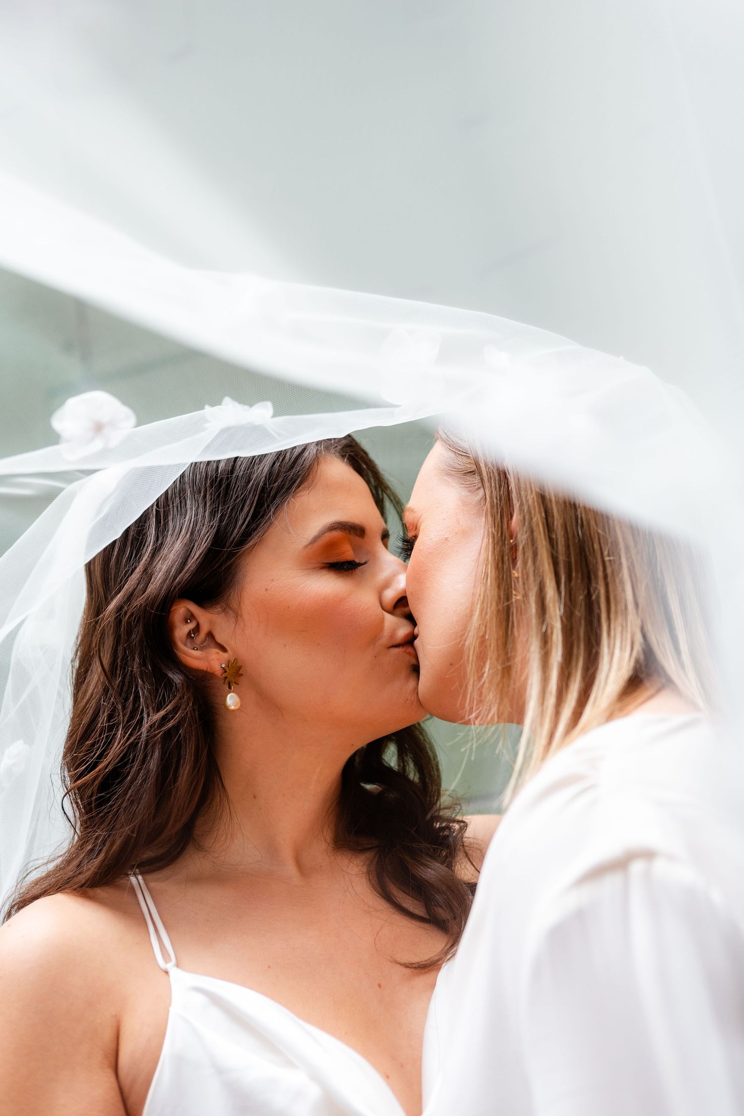 Romantic moment shared under flowing white veil during wedding ceremony.