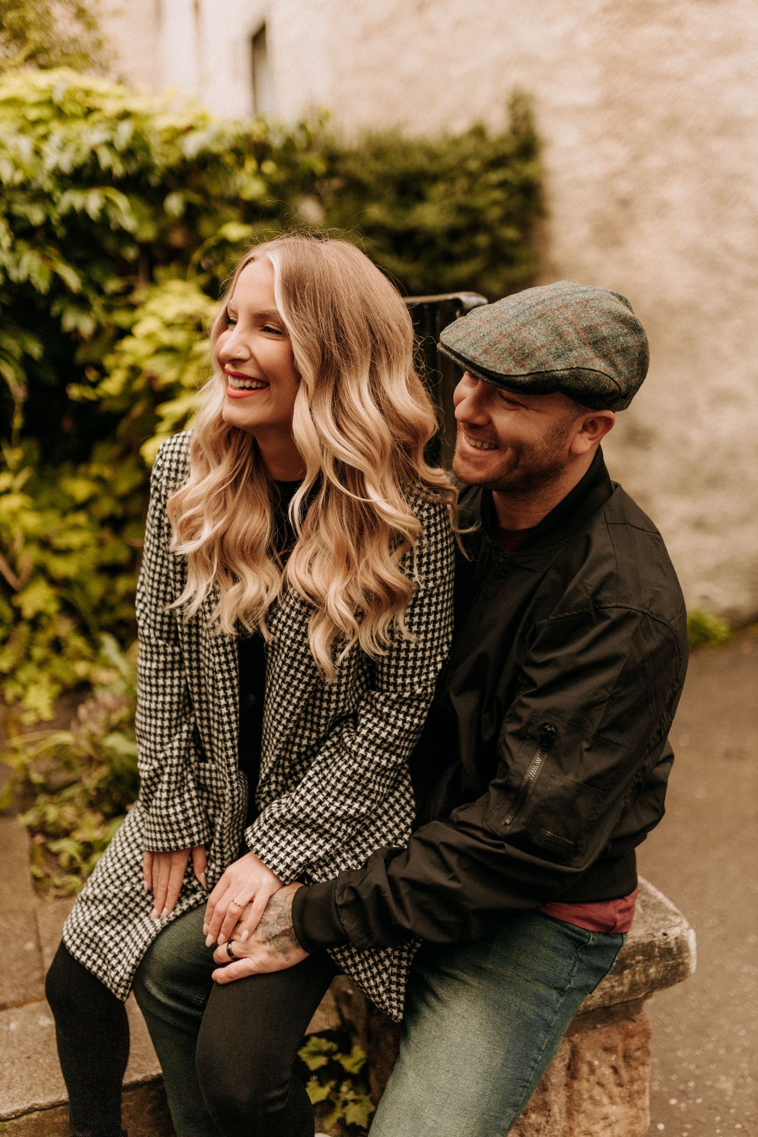 Couple sharing laughter and intimate moments on stone steps with greenery in background.
