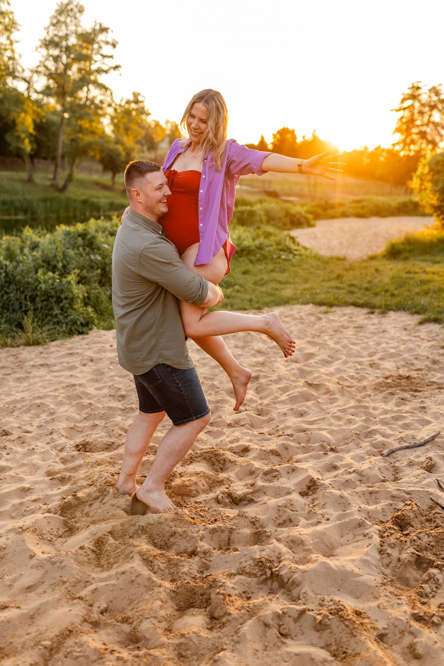 Couple playing and laughing together on sandy beach during golden sunset.