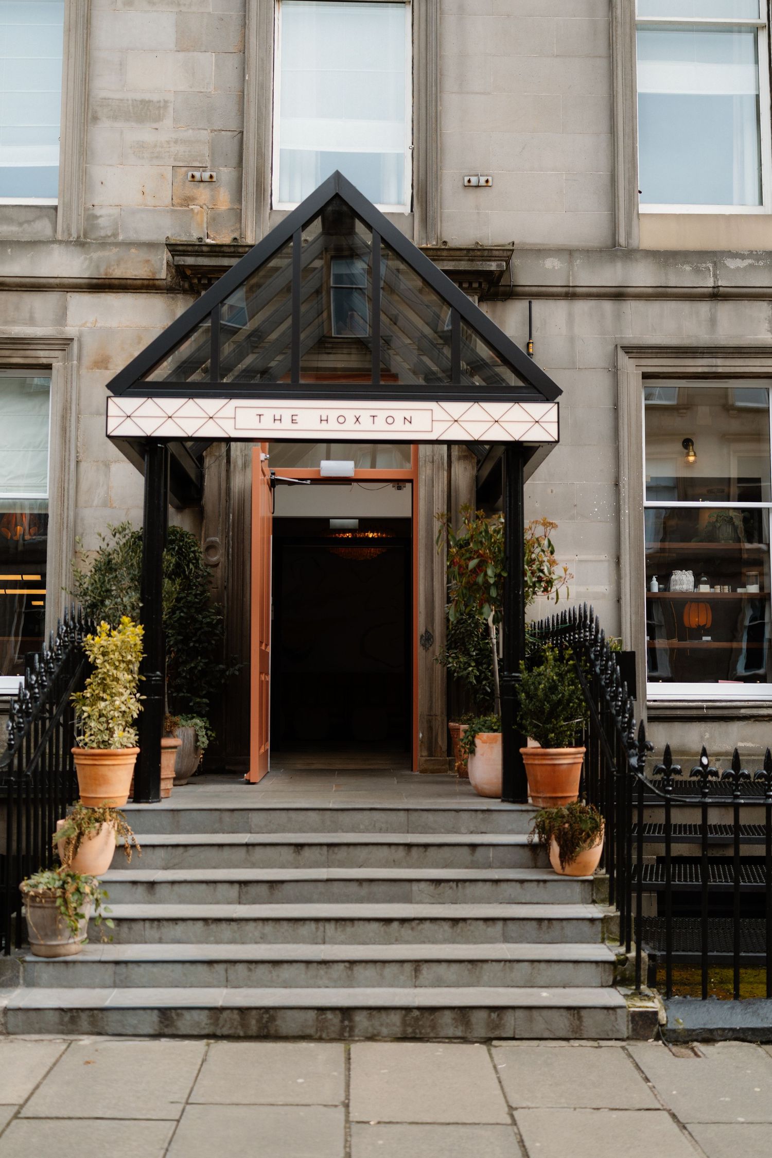 Exterior entrance of The Hoxton hotel in Edinburgh with stone facade, potted plants, and open doors.