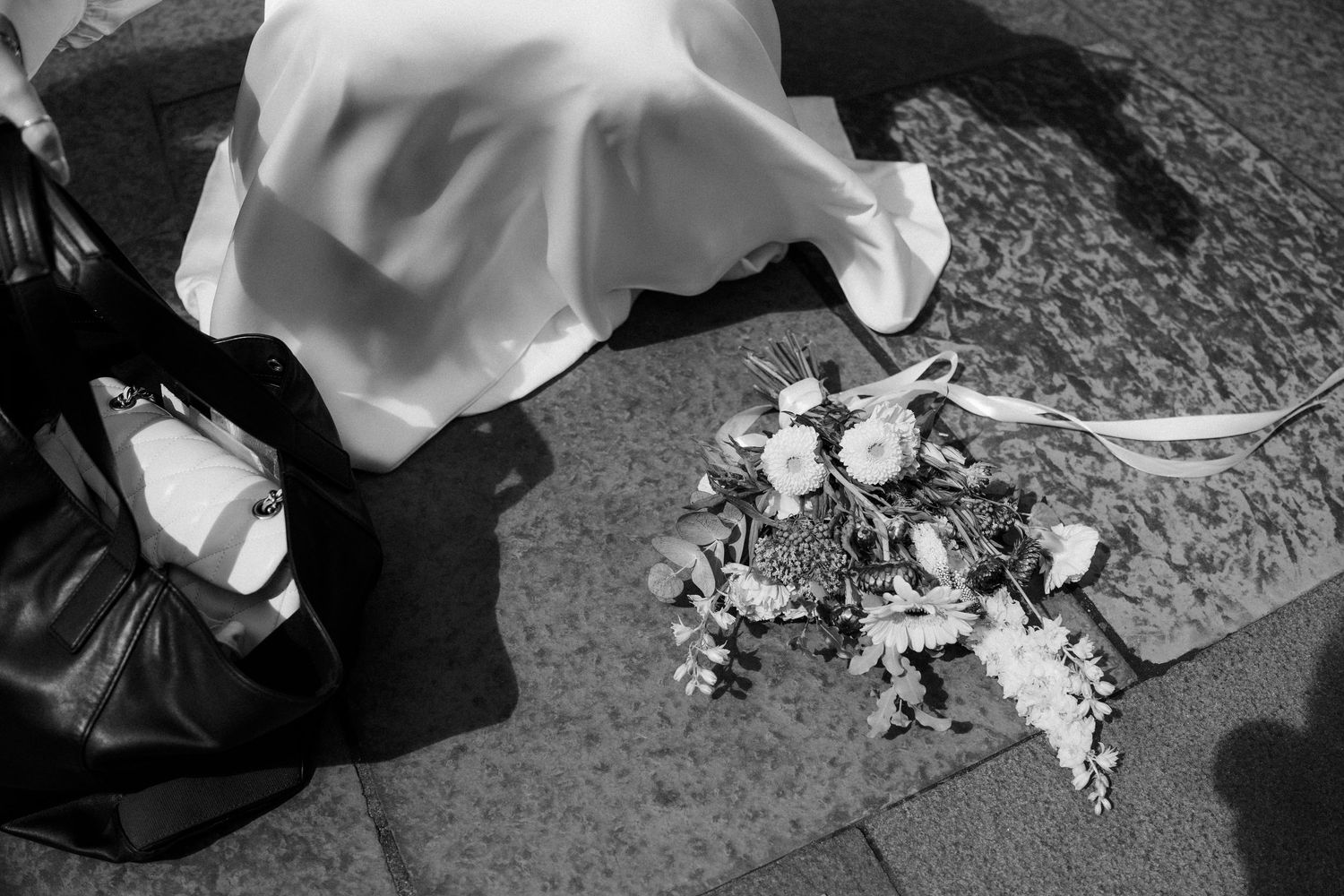 Black and white overhead shot of bridal bouquet and handbag on stone pavement.