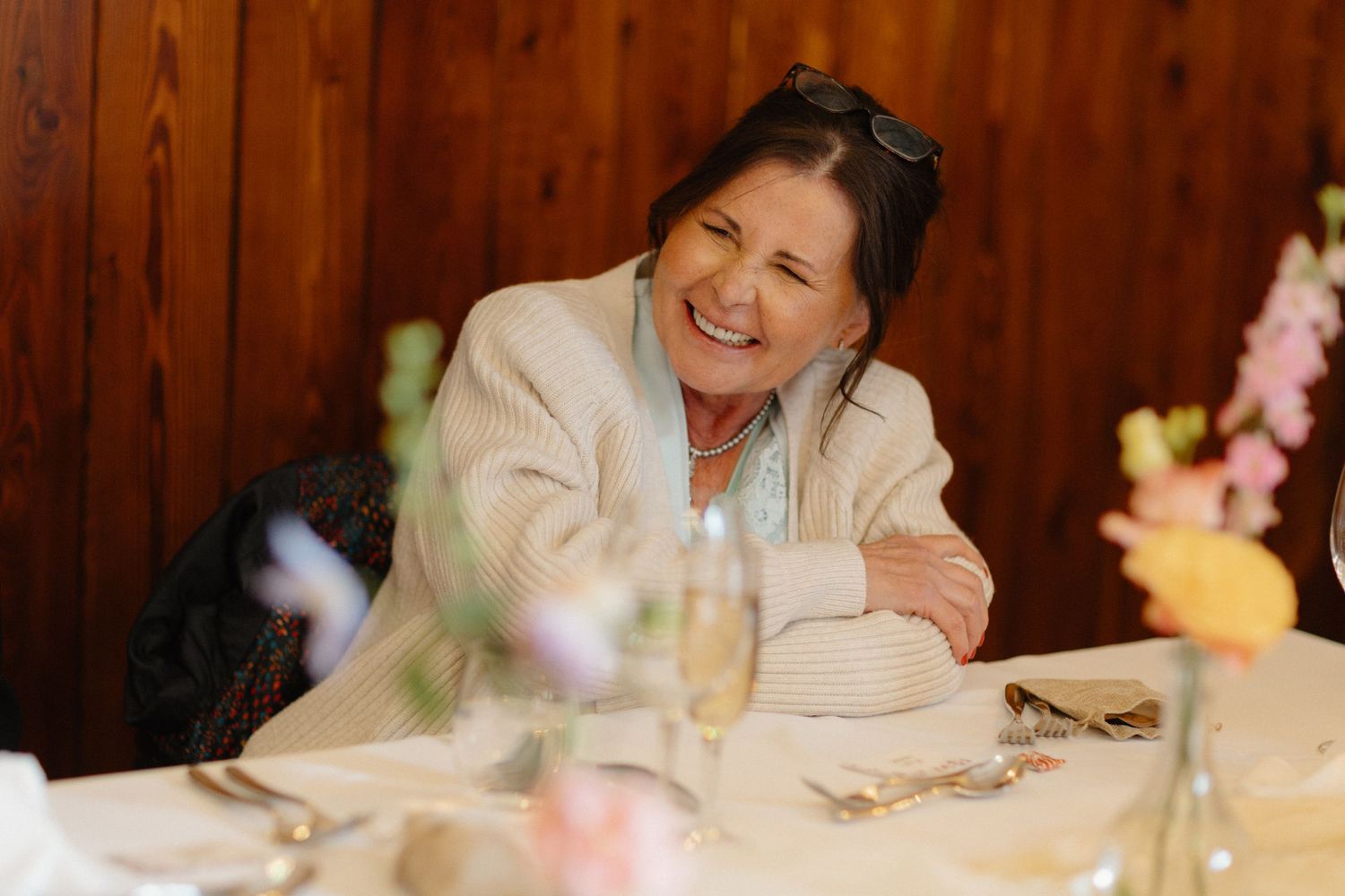 Joyful older woman laughing at a wedding reception table with champagne and flowers.
