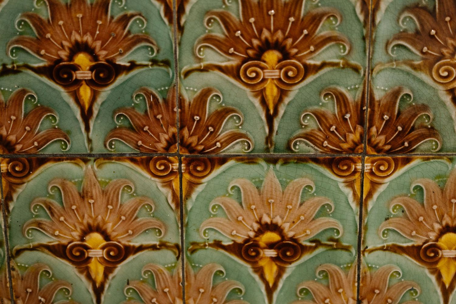 Ornate ceramic tiles featuring Art Nouveau floral patterns in turquoise, brown, and gold with symmetrical scrollwork designs.