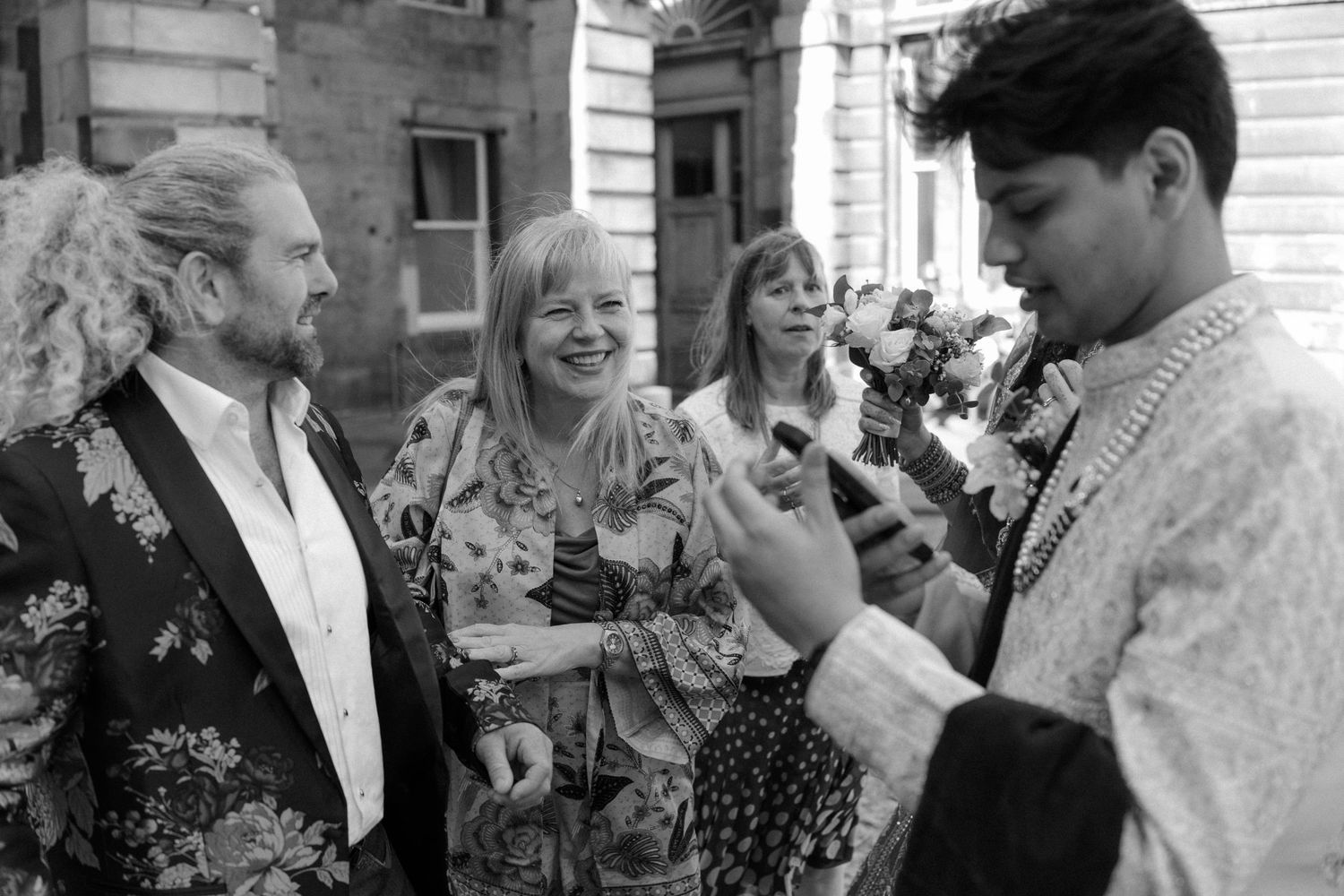 Black and white photo of four people smiling and chatting outdoors at a social gathering.