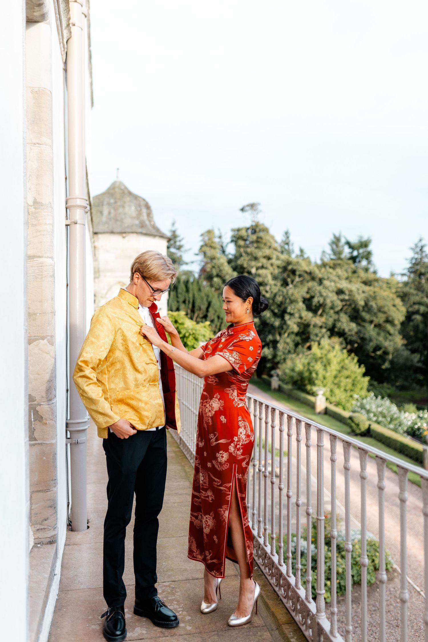 Couple in traditional Chinese and Western attire share a moment on an outdoor balcony.