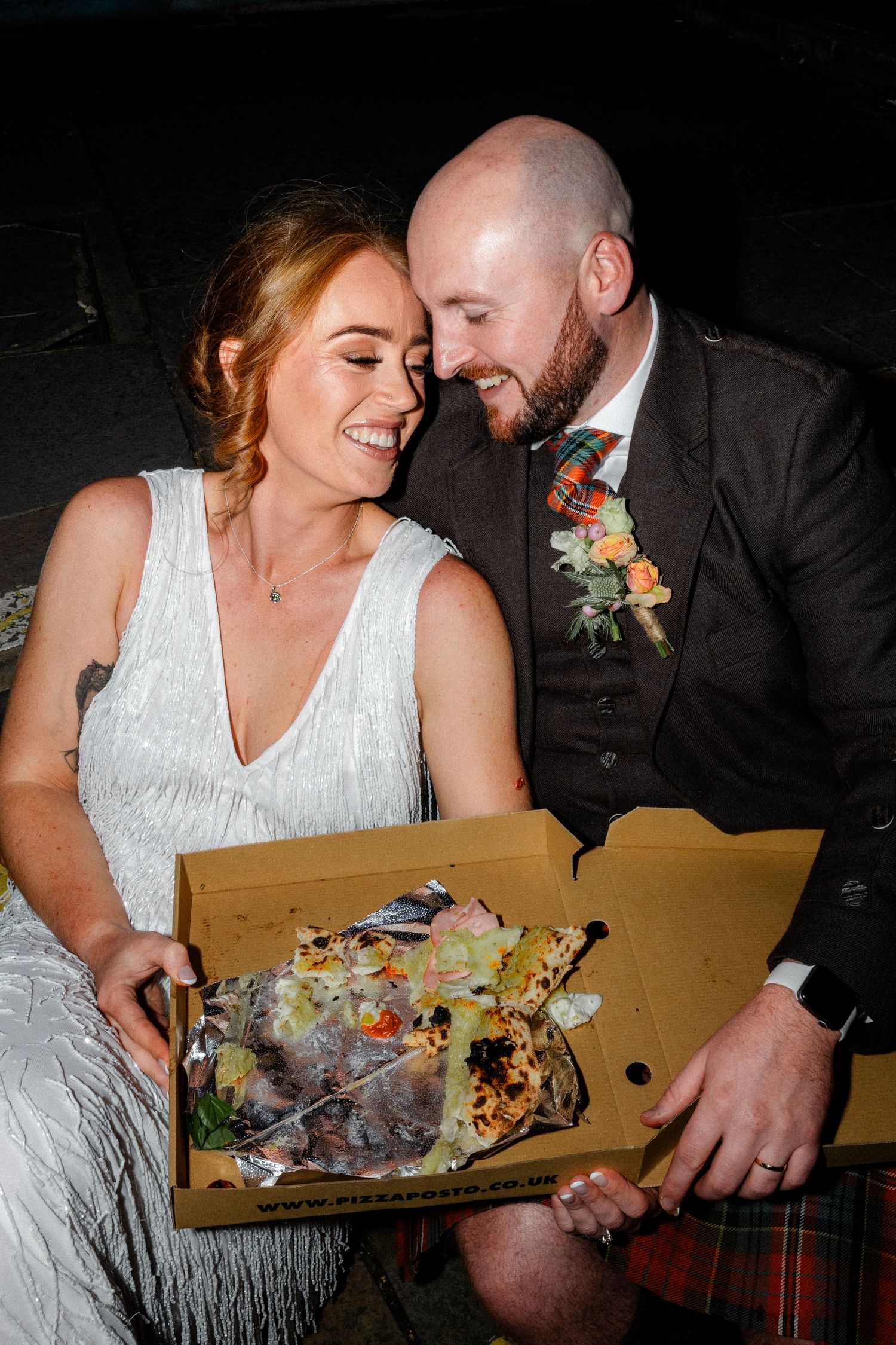 A couple sharing a joyful moment while looking at pizza in a cardboard box.